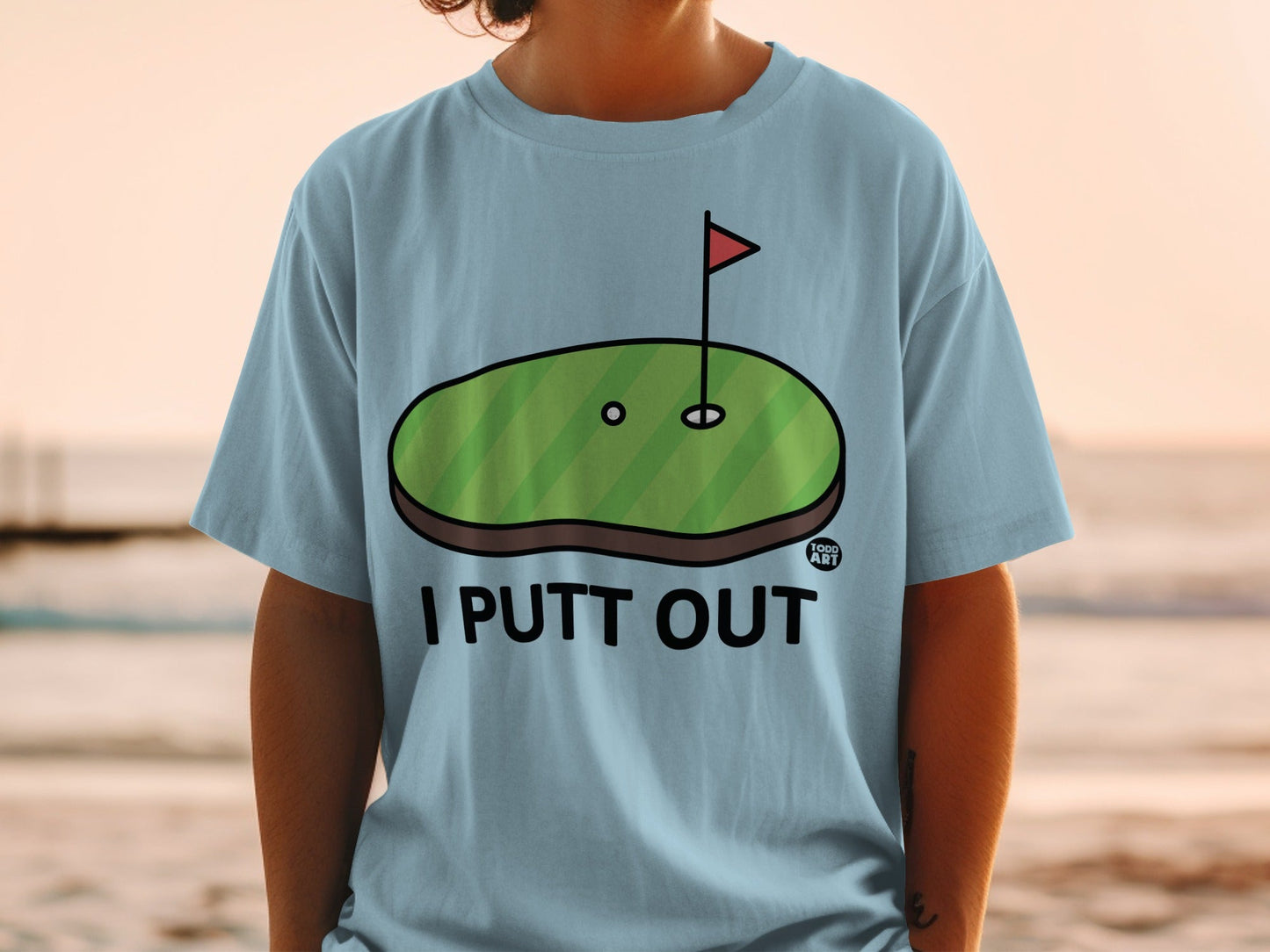 Light blue t-shirt with "I Putt Out" text and a cartoon golf green with a flag.