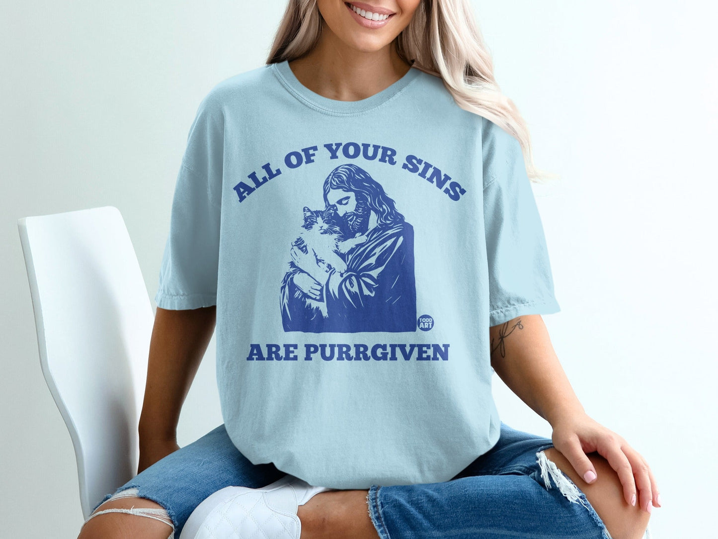 Light blue t-shirt with blue text "ALL OF YOUR SINS ARE PURRGIVEN" and a Jesus-like figure holding a cat.