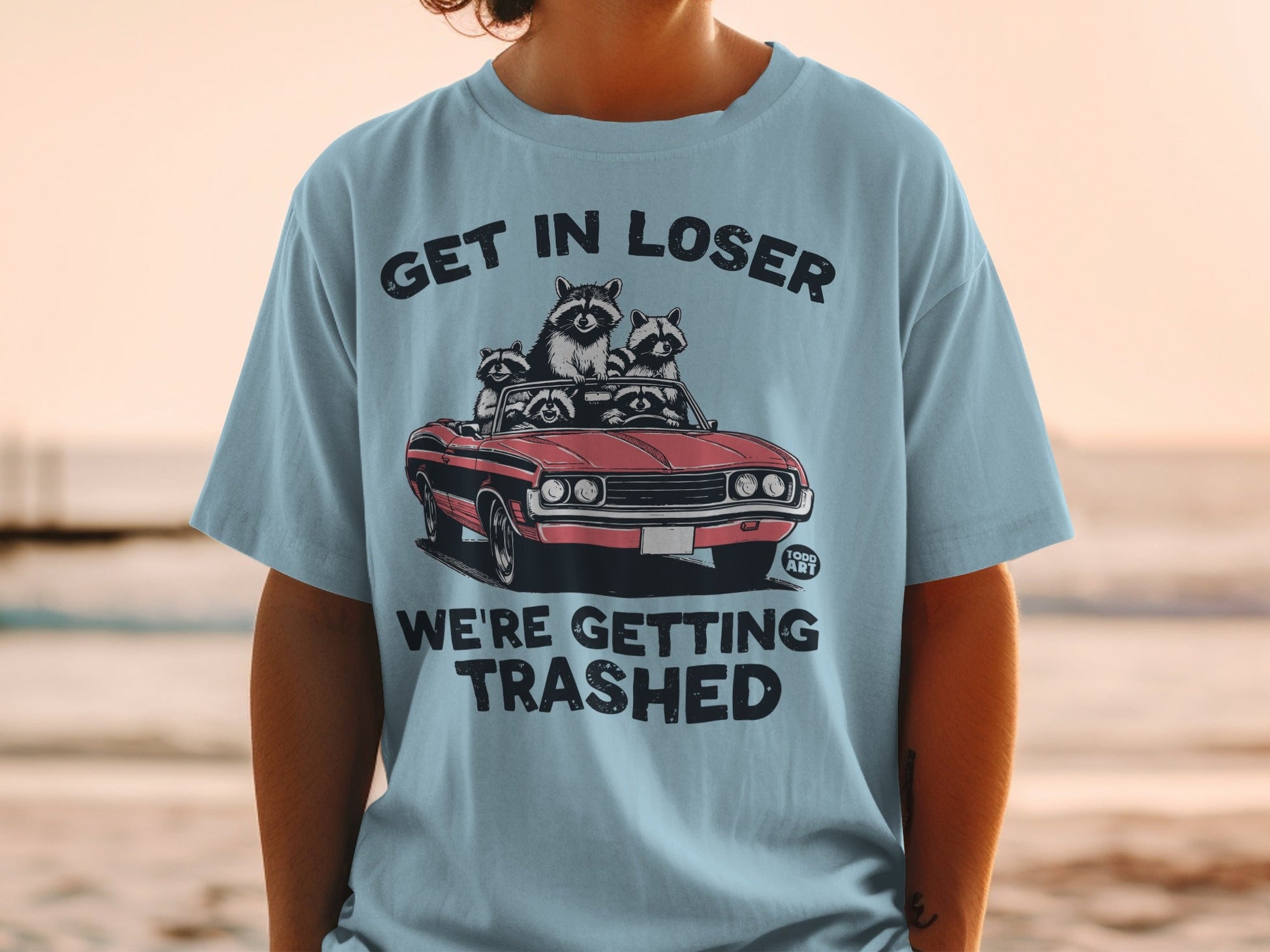 T-shirt with raccoons in a convertible, text "GET IN LOSER WE'RE GETTING TRASHED".