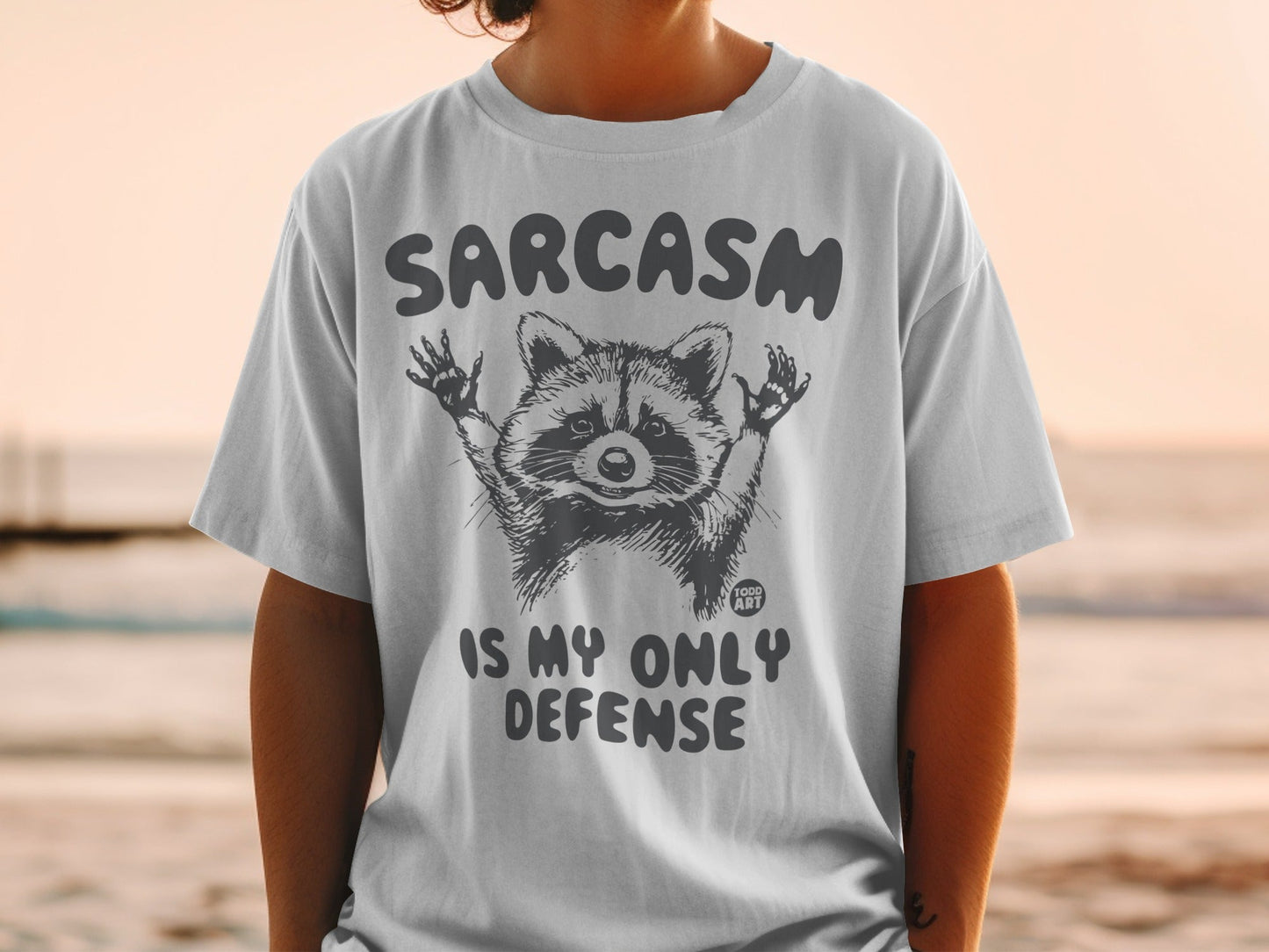 T-shirt with raccoon graphic and text "Sarcasm is my only defense."