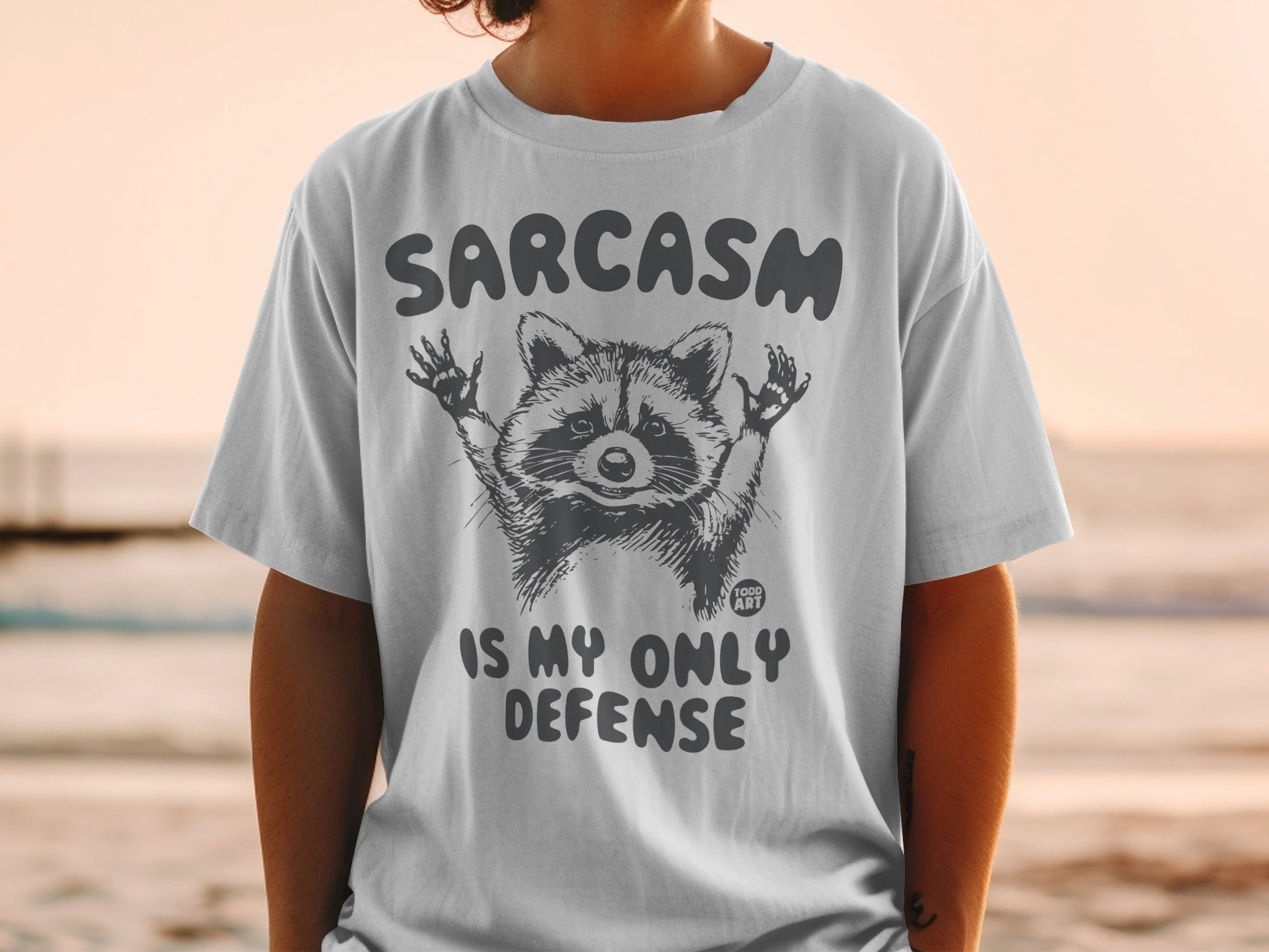 T-shirt with raccoon graphic and text "Sarcasm is my only defense."
