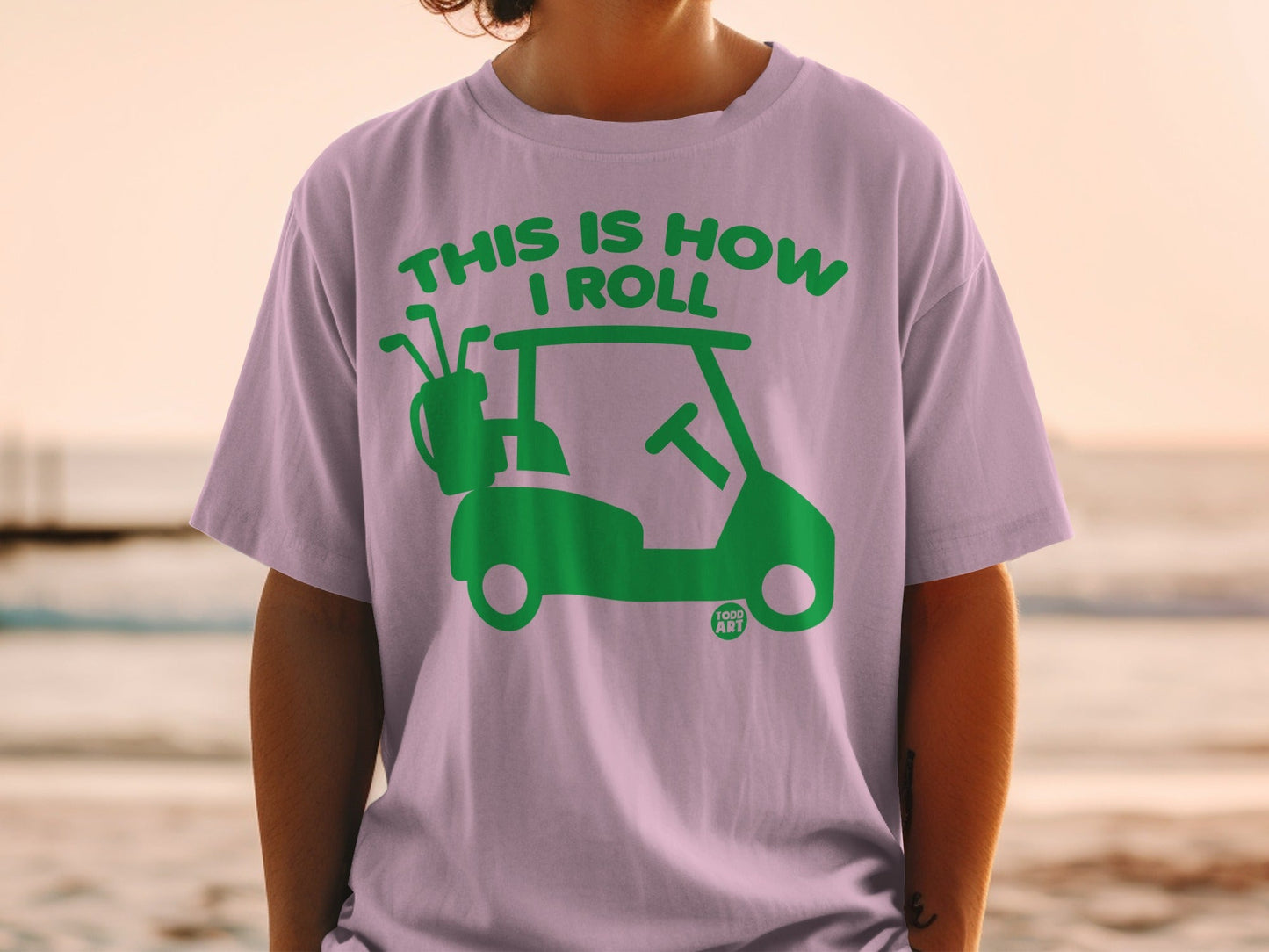 Green golf cart graphic with "THIS IS HOW I ROLL" text on a purple t-shirt.