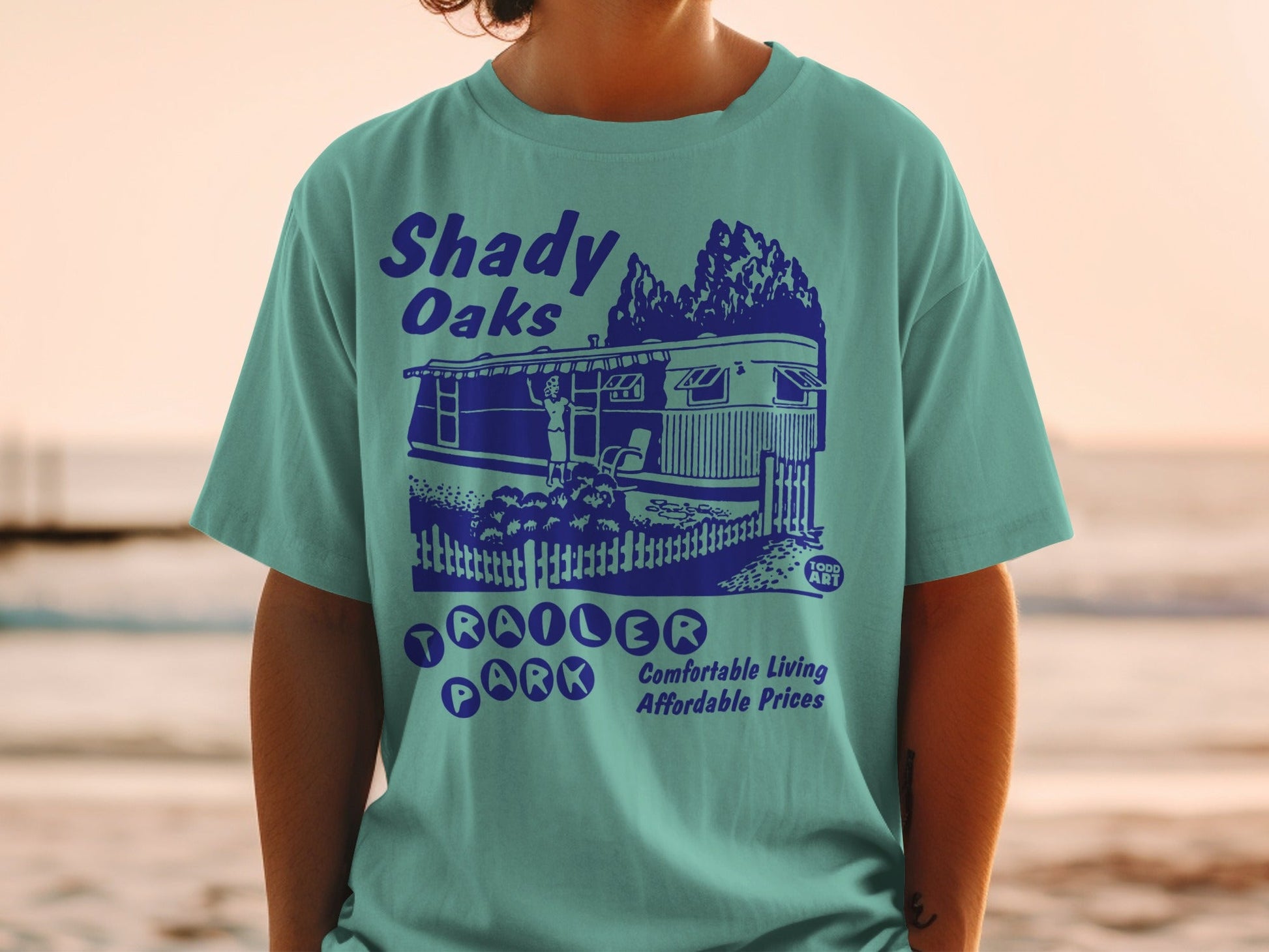 Teal t-shirt with "Shady Oaks Trailer Park" graphic depicting a trailer and text.