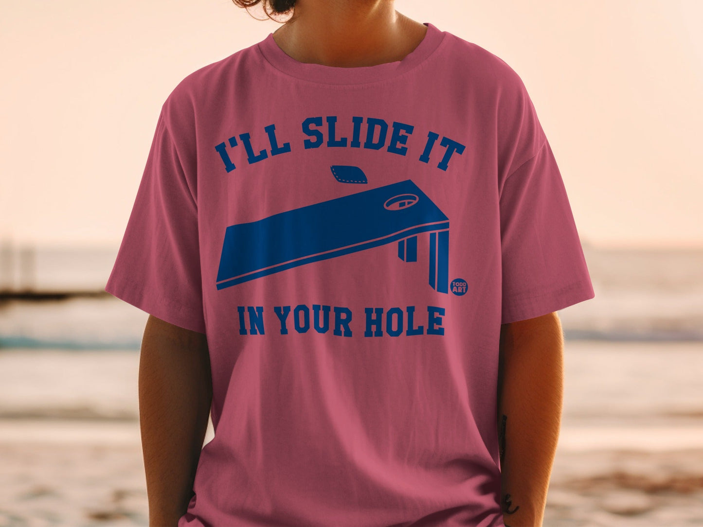 Pink t-shirt with "I'll slide it in your hole" text and cornhole board graphic.
