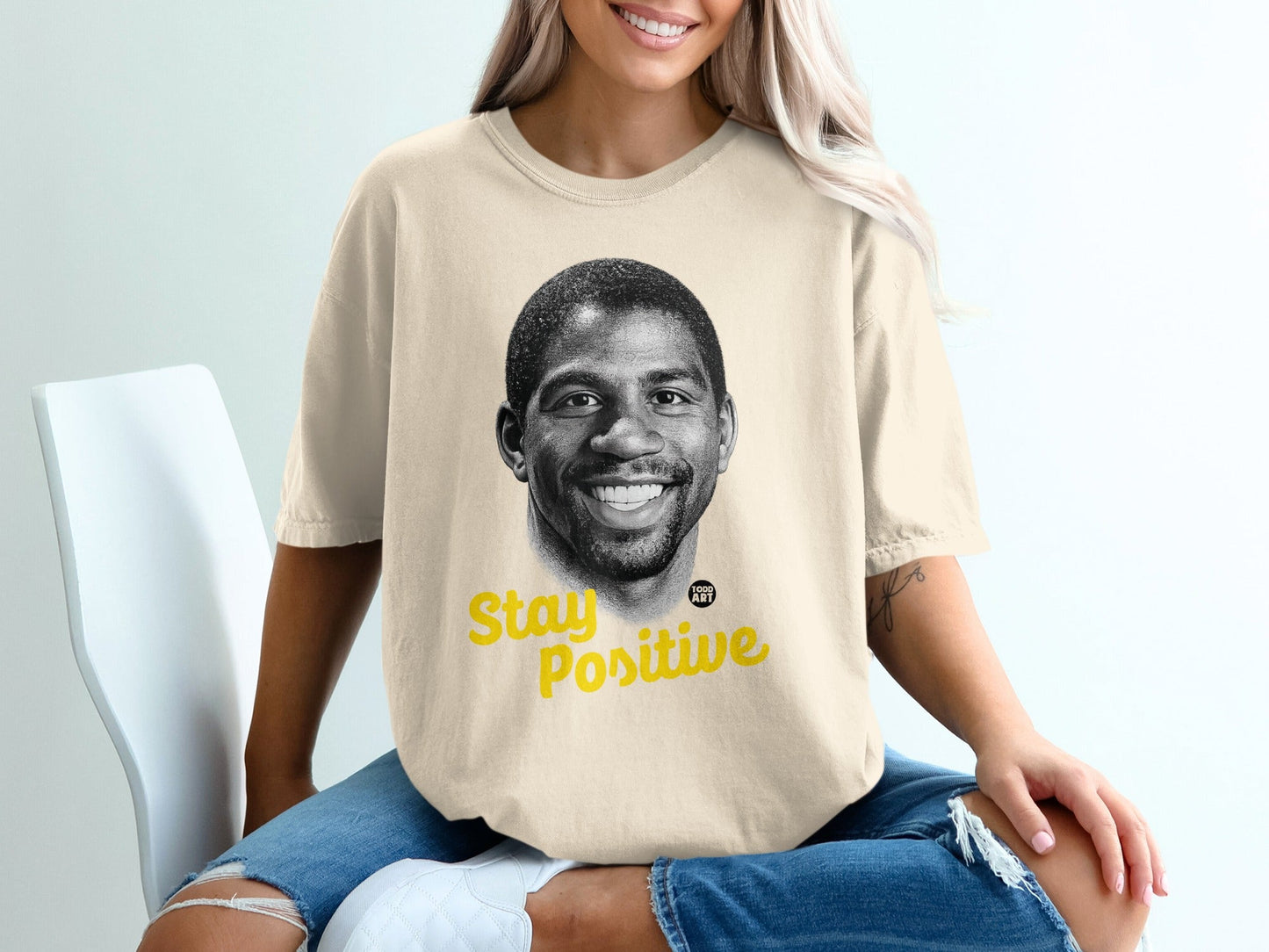 Cream t-shirt with Magic Johnson's smiling face and "Stay Positive" text.