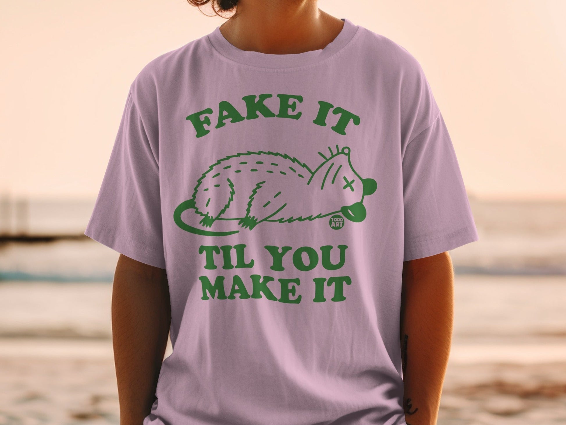 Purple t-shirt with "Fake It Til You Make It" text and a cartoon opossum.