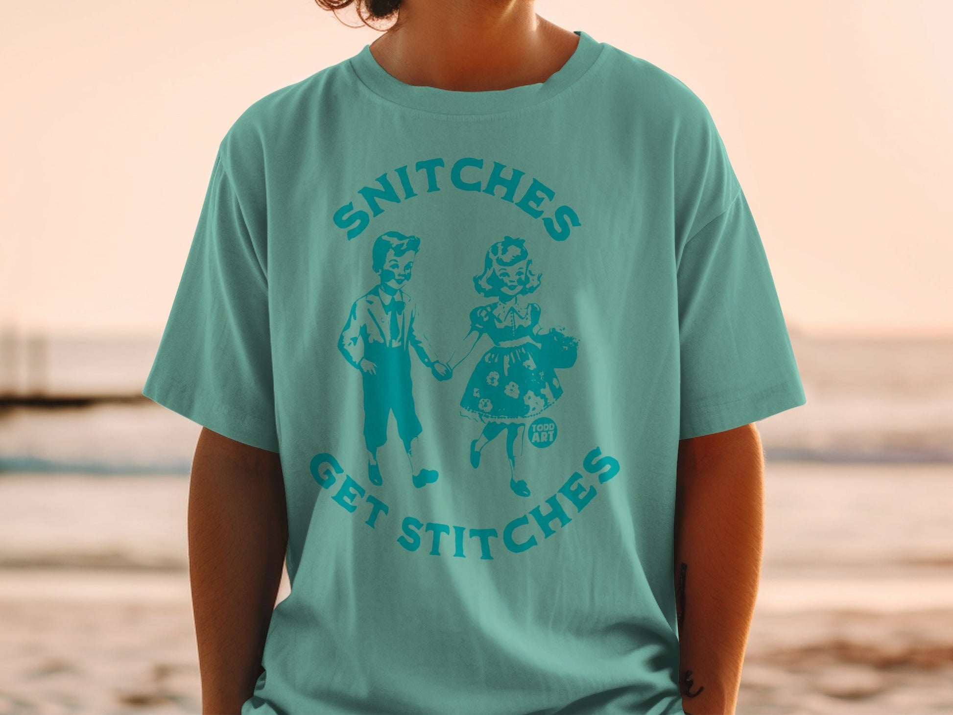 Teal t-shirt with graphic of two vintage children and text "SNITCHES GET STITCHES".