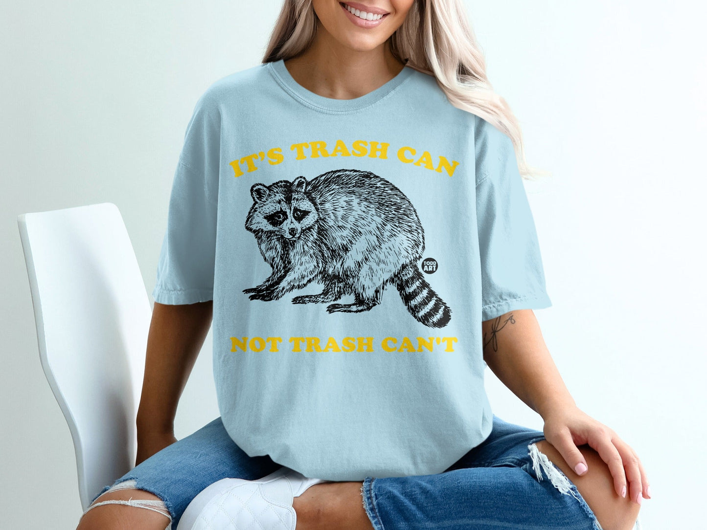 Light blue t-shirt with raccoon graphic and "It's Trash Can Not Trash Can't" text.