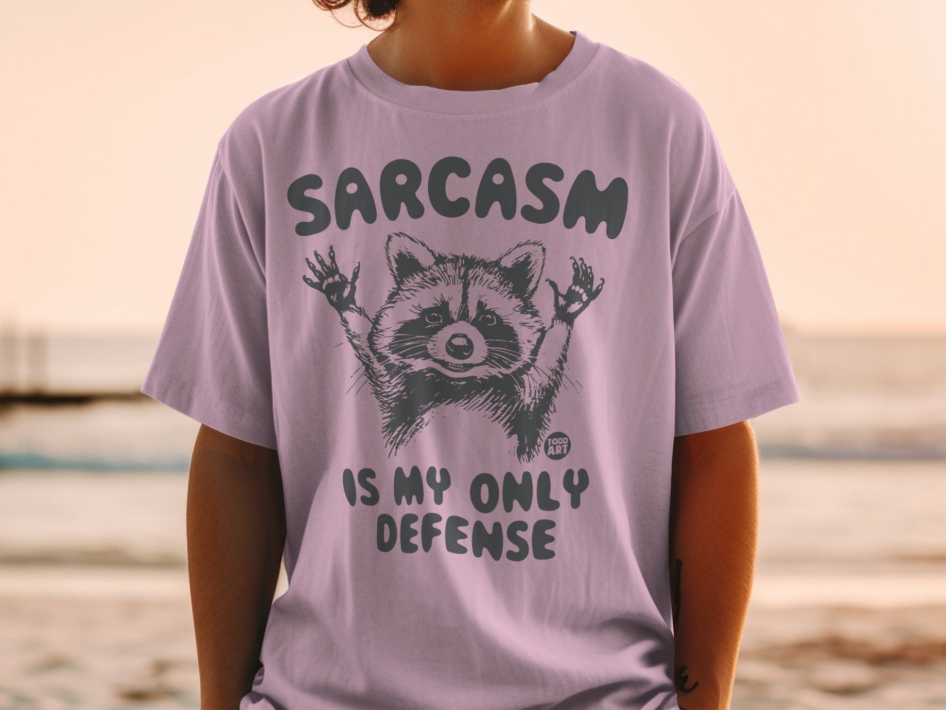T-shirt with a raccoon graphic and text "SARCASM IS MY ONLY DEFENSE".