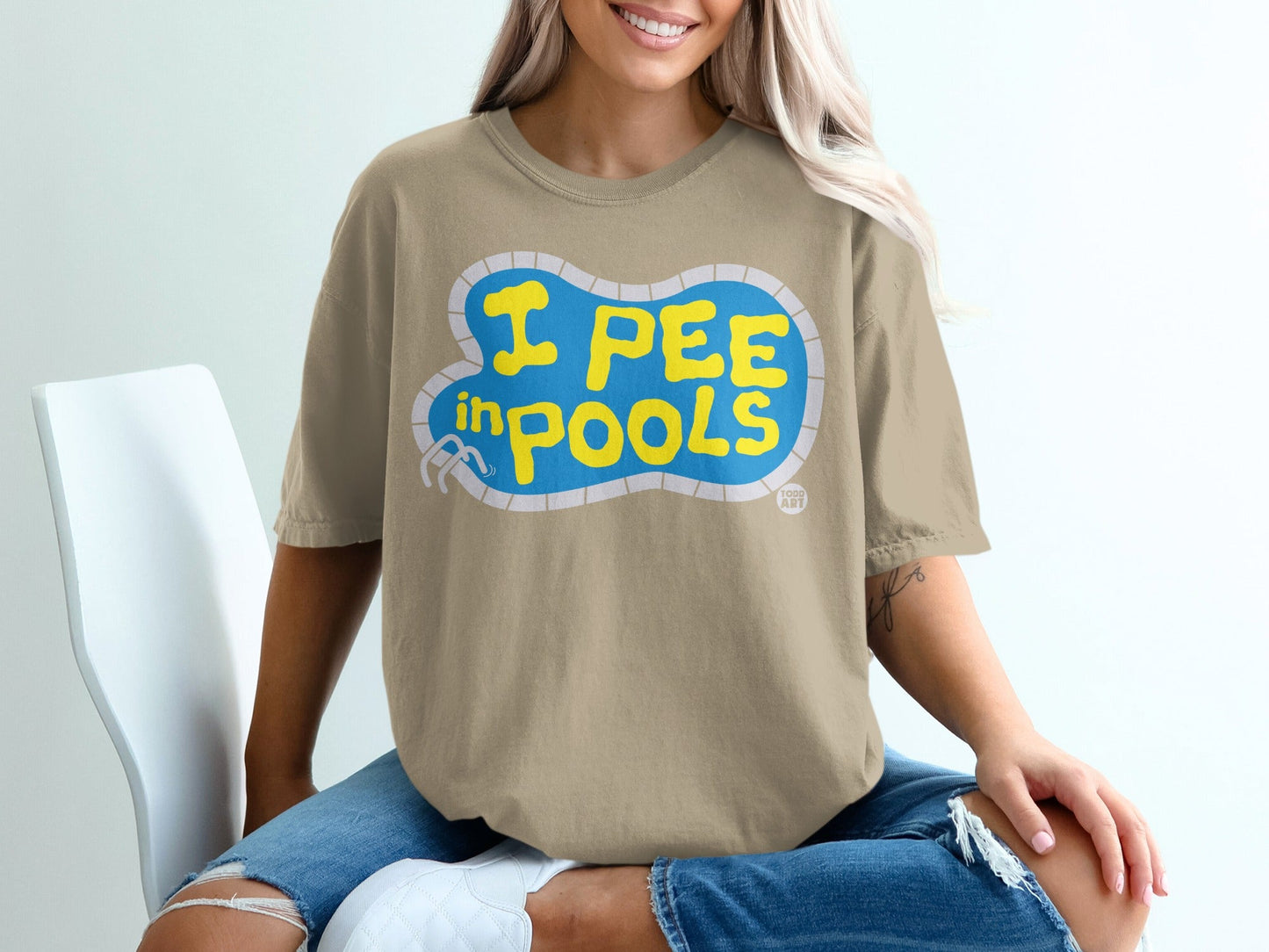Tan t-shirt with "I PEE IN POOLS" text in yellow within a blue pool graphic.