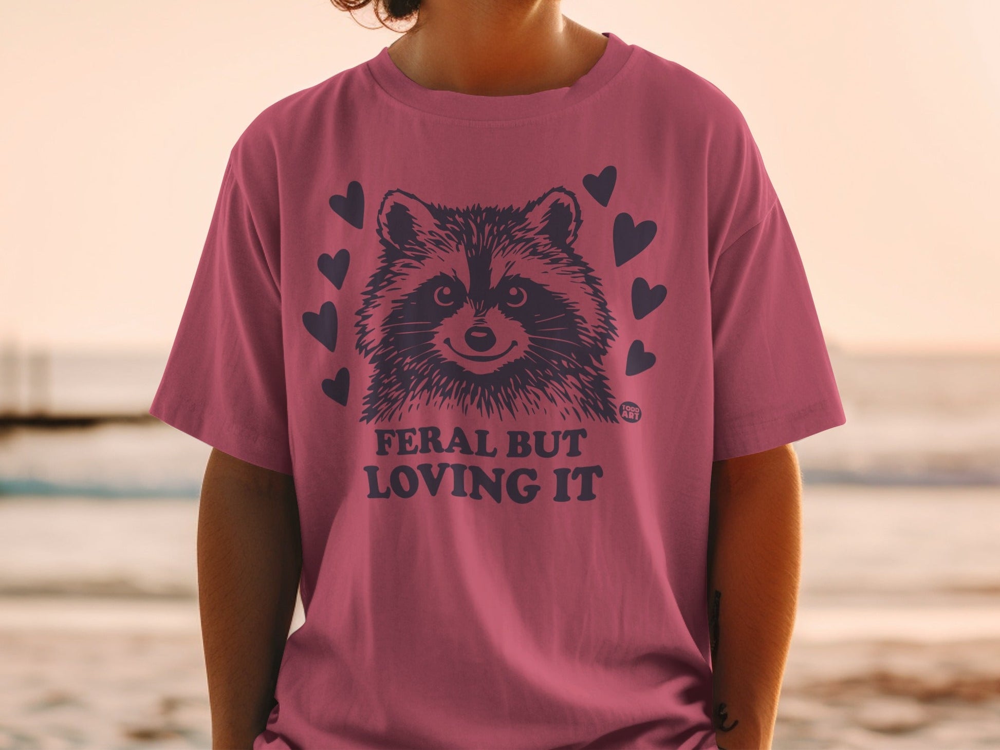Pink t-shirt with raccoon graphic and "Feral but Loving It" text.