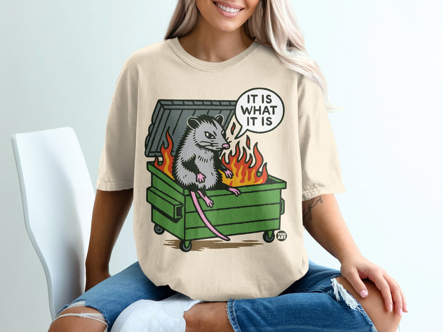 Opossum in burning dumpster with "IT IS WHAT IT IS" speech bubble.