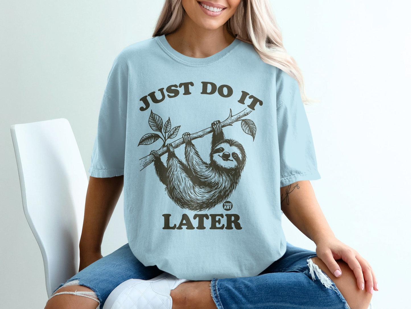 Light blue t-shirt with sloth on a branch and text "JUST DO IT LATER".