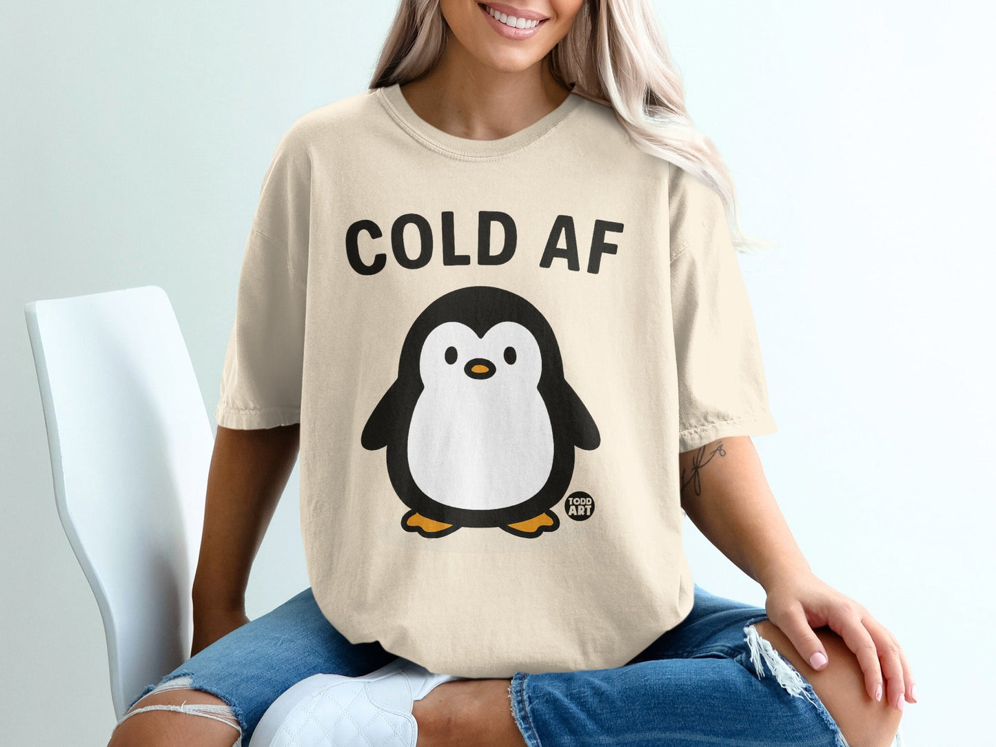 Cream t-shirt with "COLD AF" text and a cartoon penguin graphic.