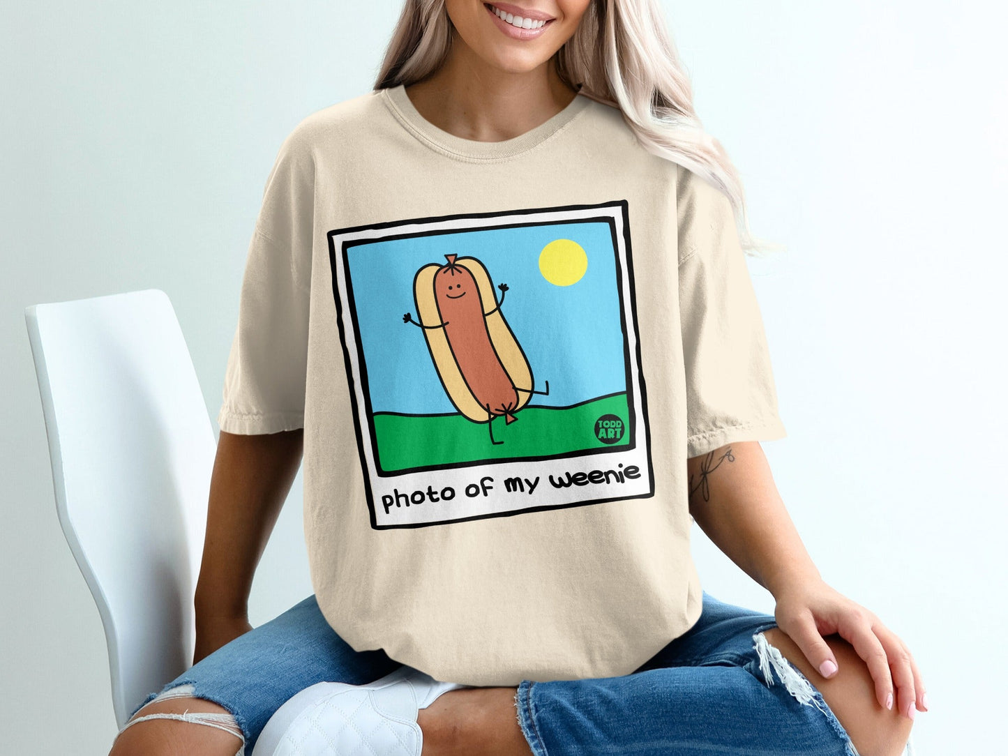 Cartoon hot dog with arms and legs smiling in grass with sun, text "photo of my weenie".