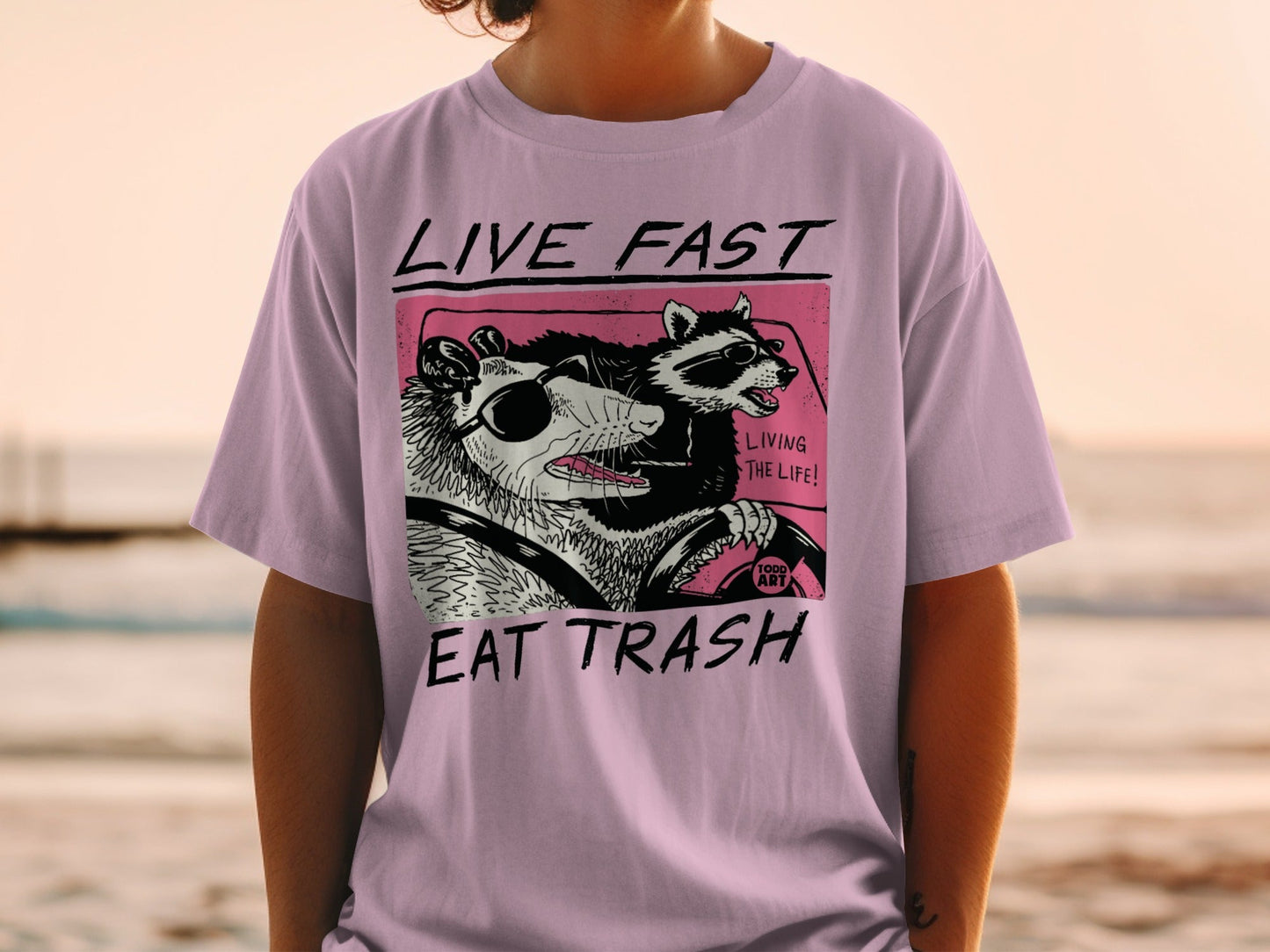 Illustration of a raccoon and possum driving a car with text "Live Fast Eat Trash."