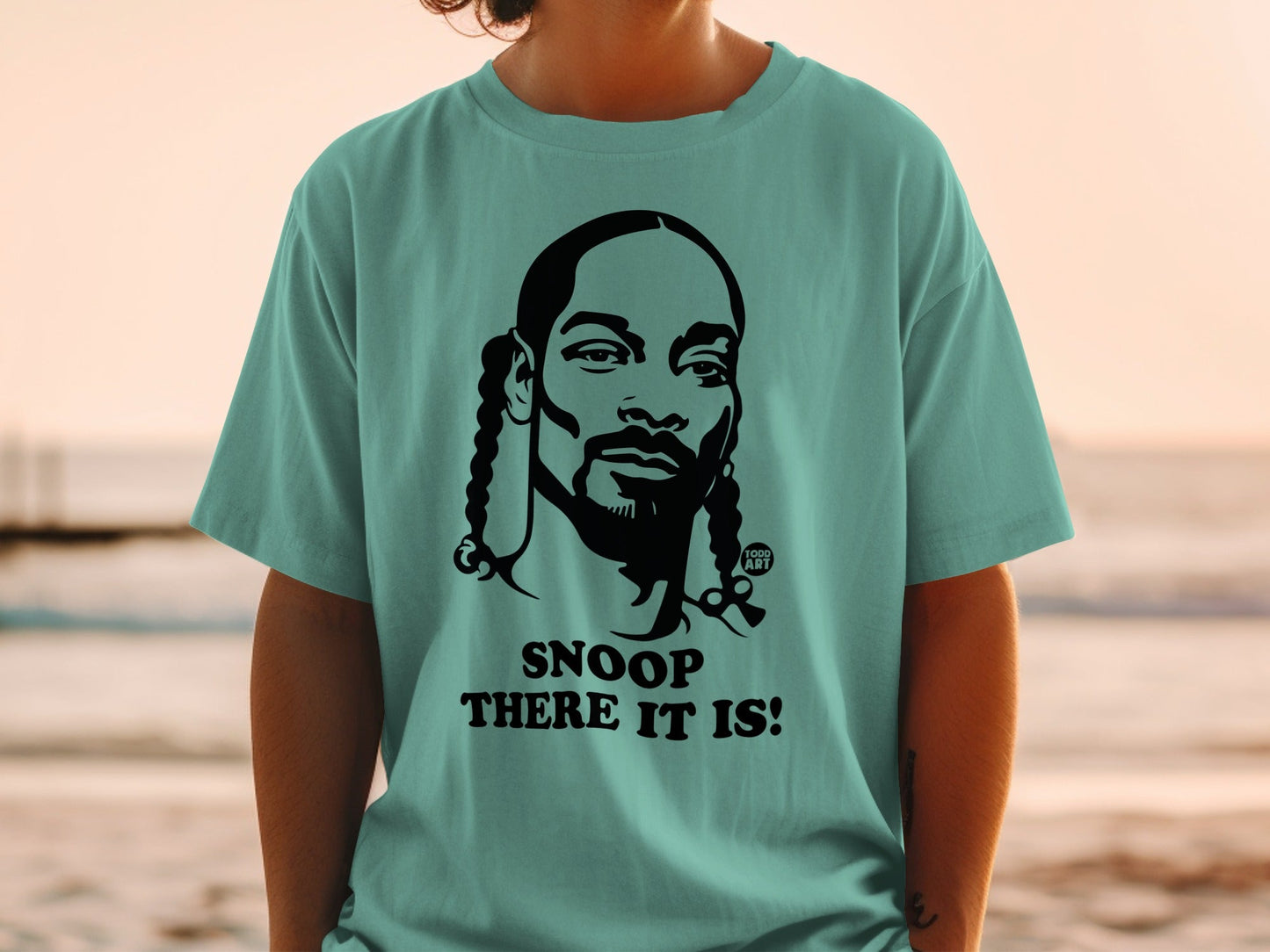 Teal t-shirt featuring a black graphic of Snoop Dogg with text "SNOOP THERE IT IS!"