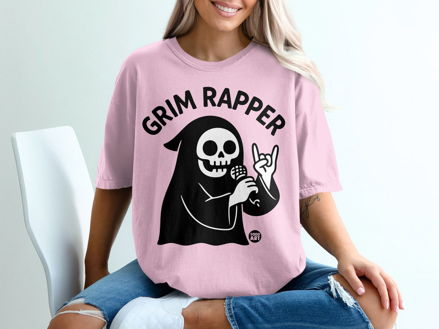 Pink t-shirt with "Grim Rapper" text and cartoon grim reaper holding microphone and making rock hand sign.