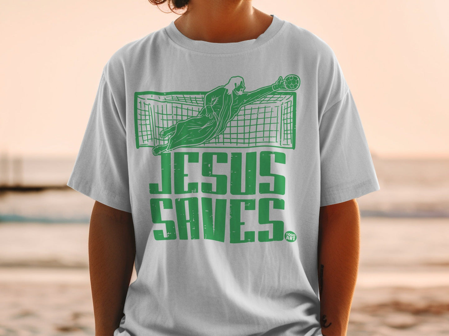 Green graphic on white t-shirt of soccer goalie saving goal, text "JESUS SAVES".
