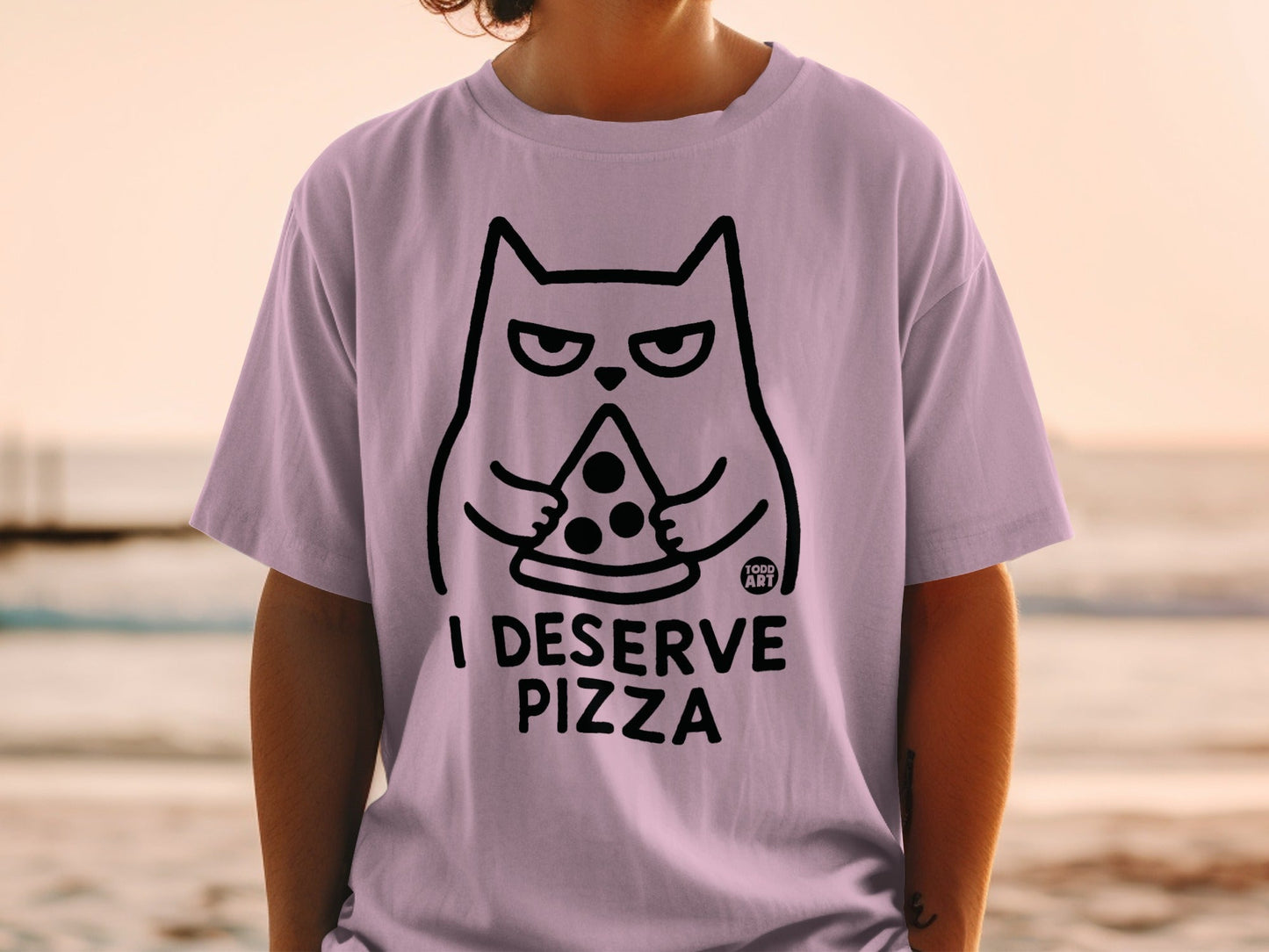Light purple t-shirt with a black line drawing of a cat holding a slice of pizza and the text "I DESERVE PIZZA".