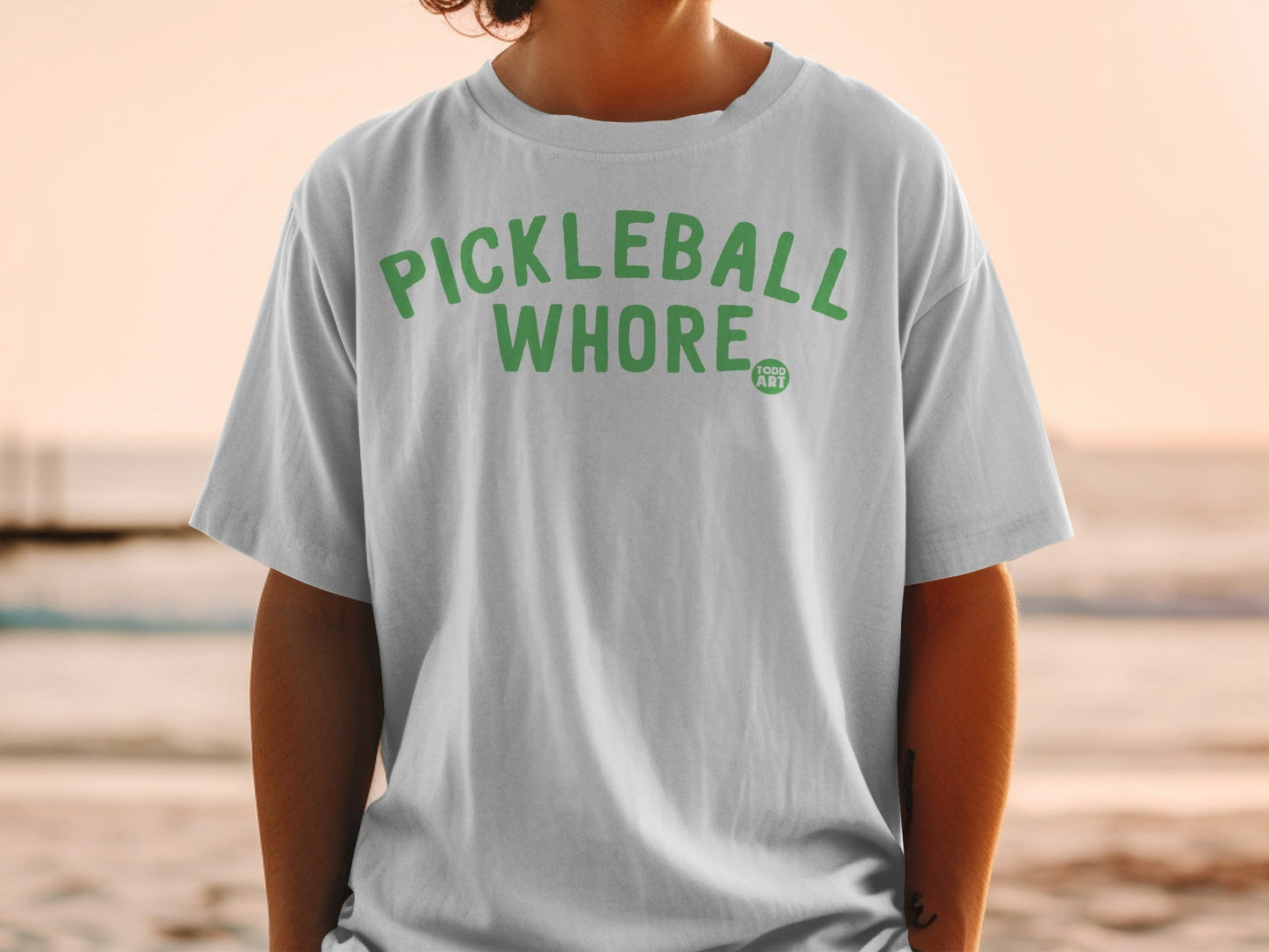 White t-shirt with "PICKLEBALL WHORE" and "1000 ART" in green text.