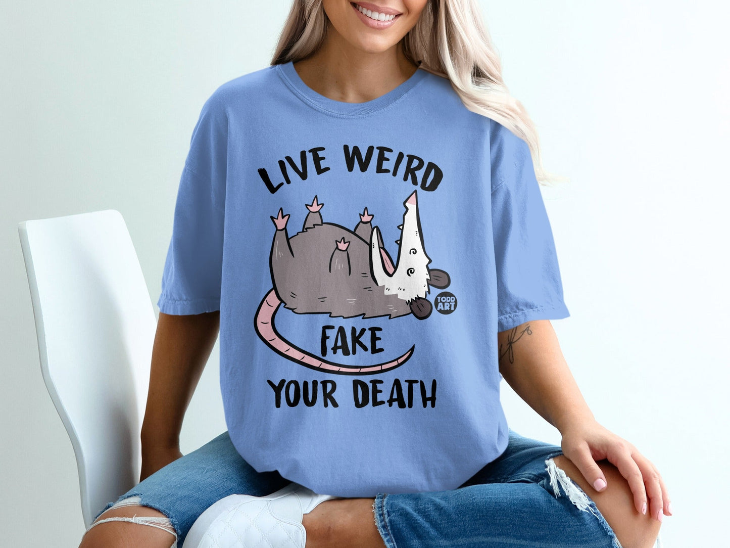 Blue t-shirt with opossum graphic and text "LIVE WEIRD FAKE YOUR DEATH".