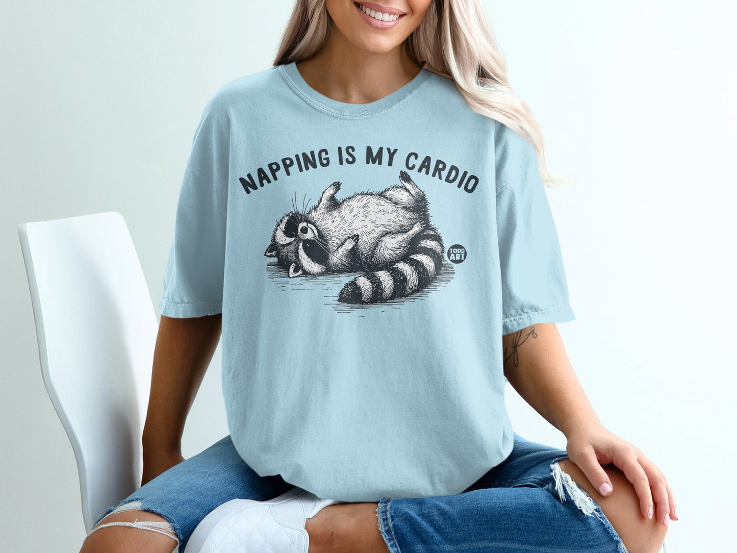 Light blue t-shirt with raccoon napping graphic and text.