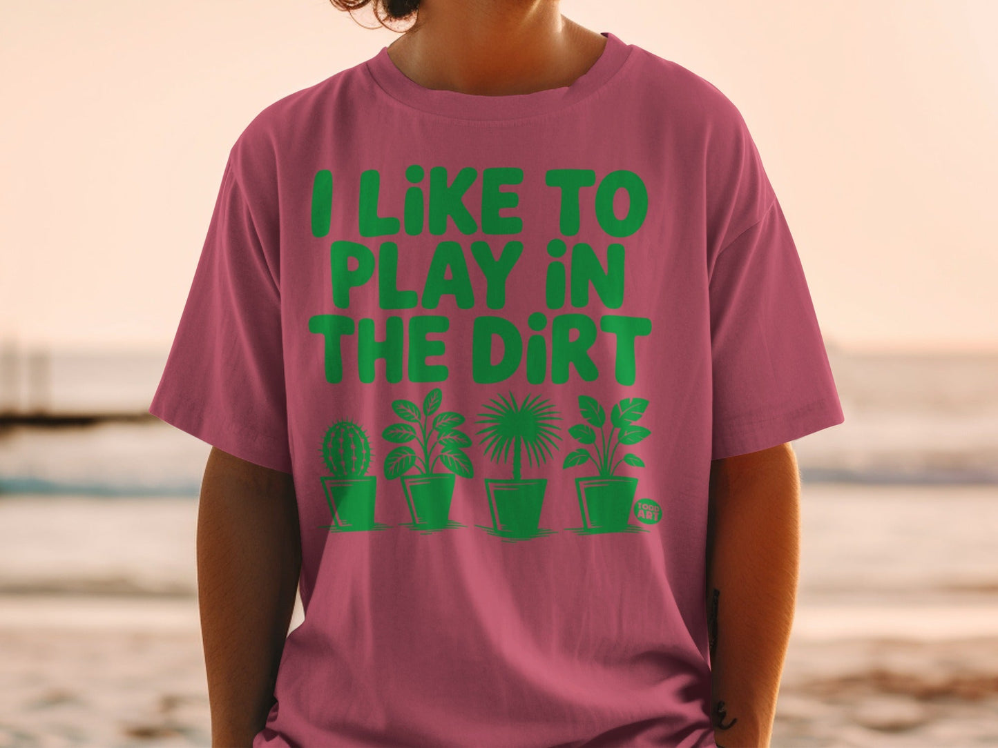 Pink t-shirt with green text "I LIKE TO PLAY IN THE DIRT" and potted plants.