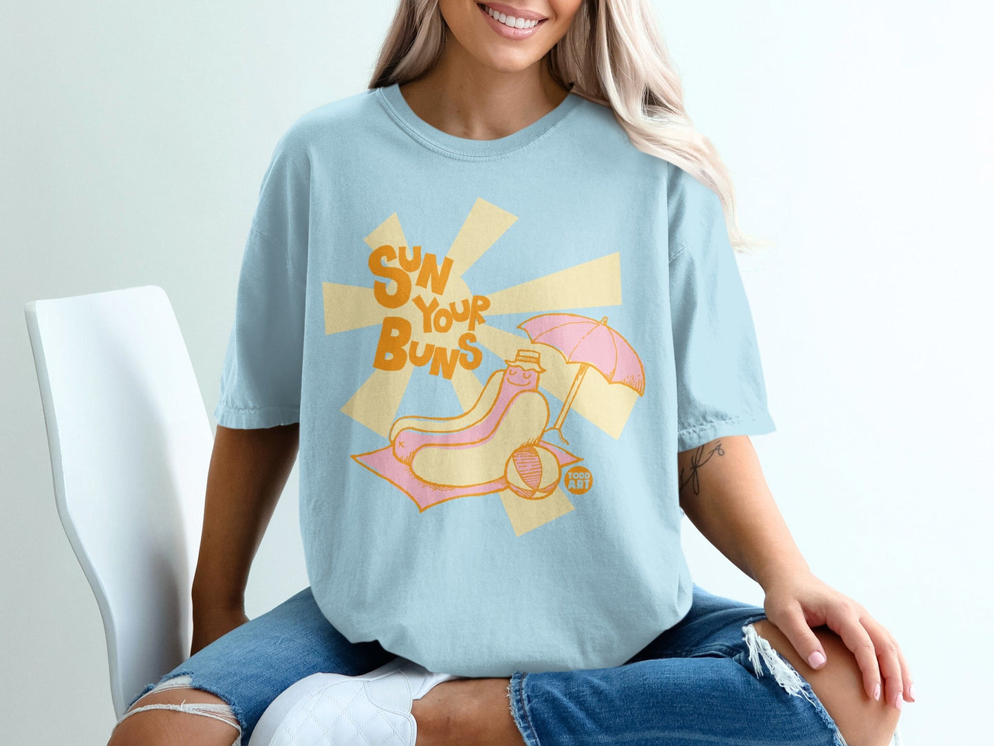 T-shirt with a hot dog under an umbrella on a beach, text "SUN YOUR BUNS".