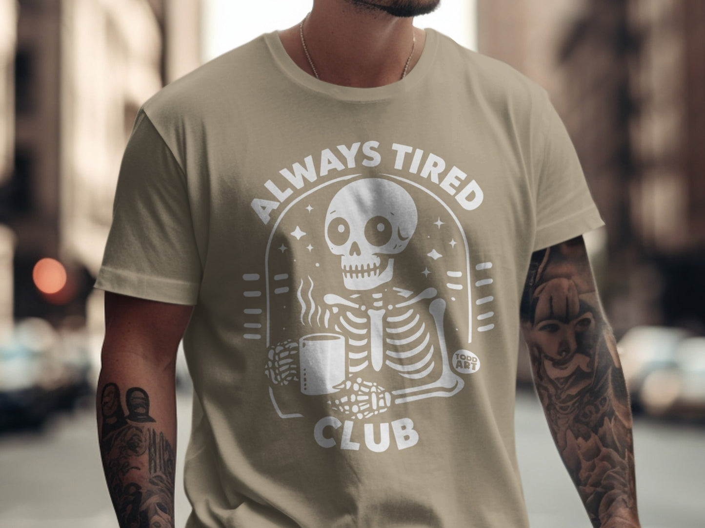 Light brown t-shirt with "ALWAYS TIRED CLUB" and skeleton holding coffee cup.