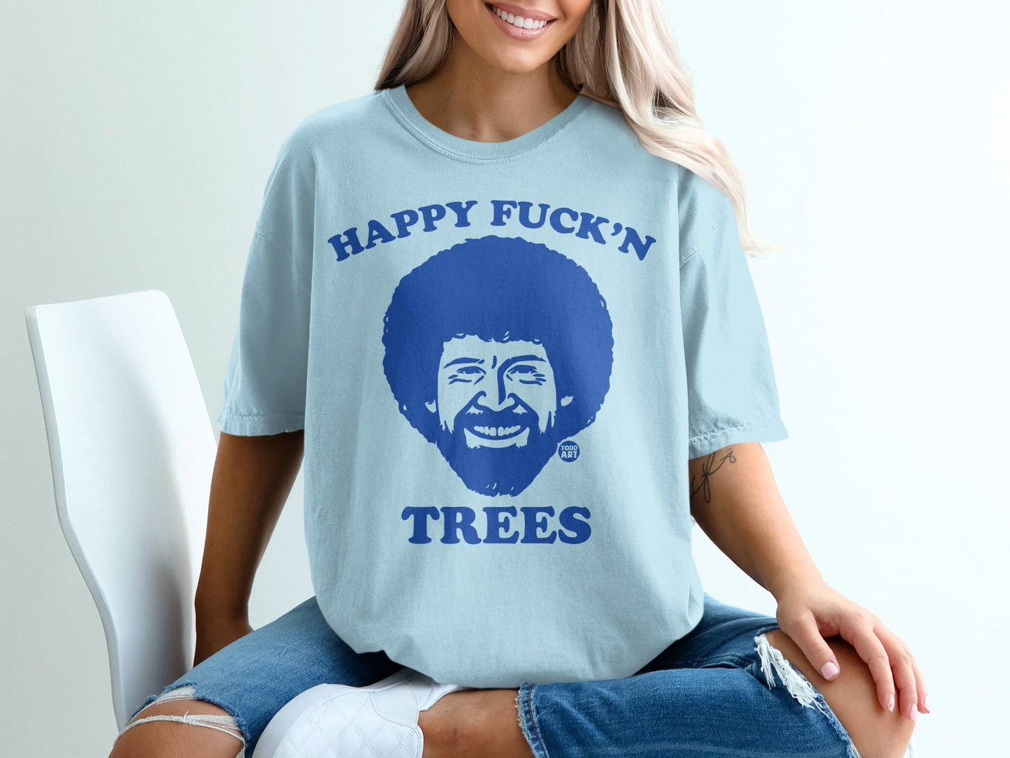 Light blue t-shirt with Bob Ross saying "Happy Fuck'n Trees".
