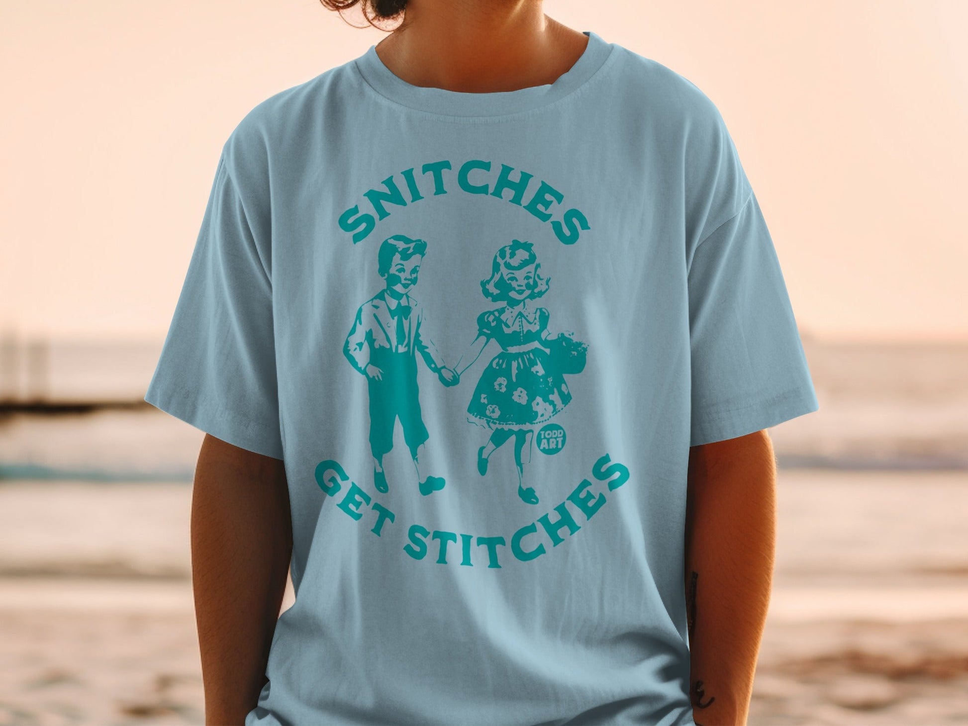 Light blue t-shirt with "Snitches Get Stitches" text and vintage couple illustration.
