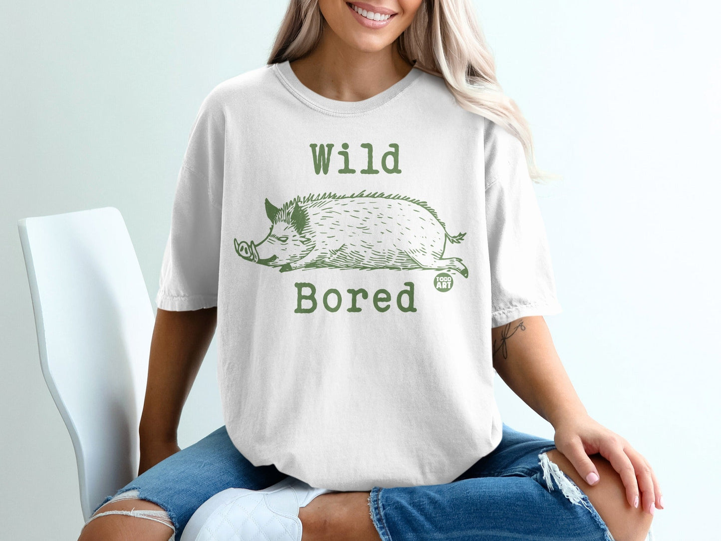 White t-shirt featuring a green graphic of a sleeping wild boar and text "Wild Bored."