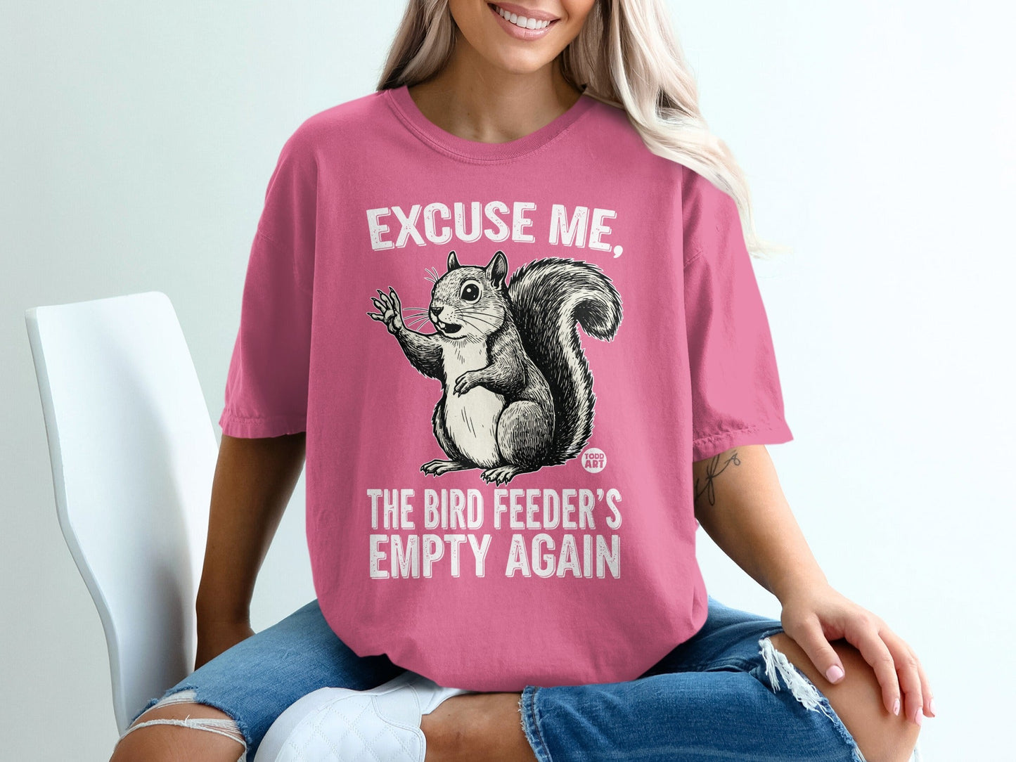 Pink t-shirt with a graphic of a squirrel saying "Excuse me, the bird feeder's empty again".