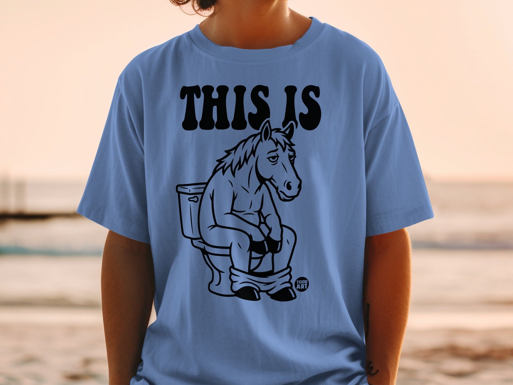 Blue t-shirt with black graphic of horse sitting on a toilet.
