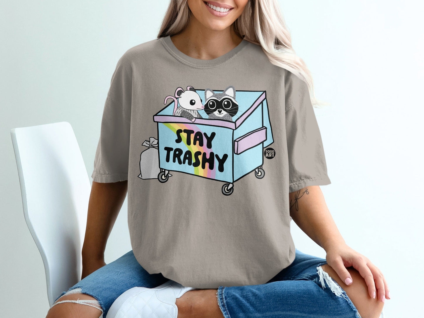 Cartoon raccoon and mouse in a trash can with rainbow and "Stay Trashy" text.