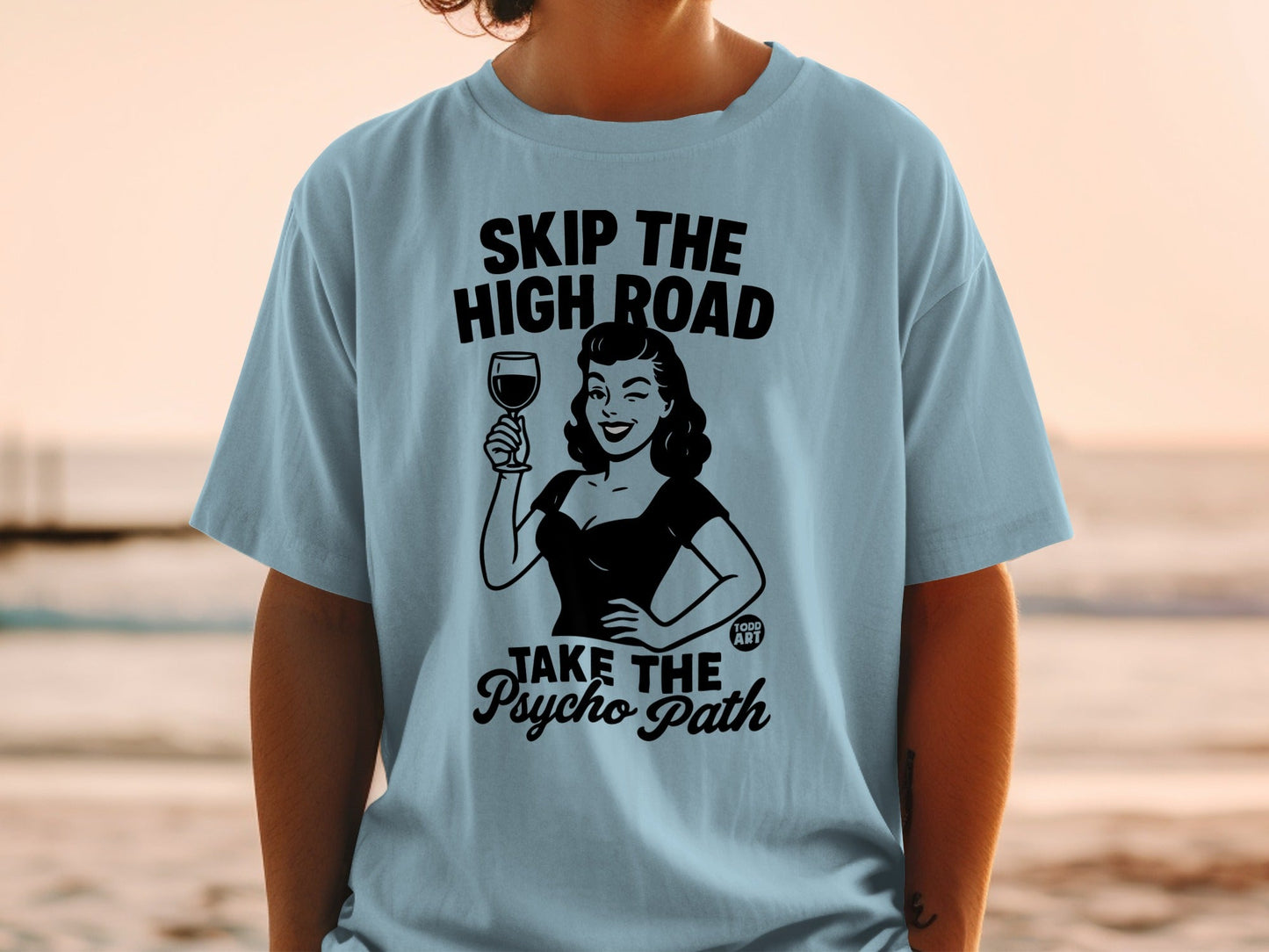 Light blue t-shirt with black graphic of woman holding wine, "SKIP THE HIGH ROAD TAKE THE PSYCHO PATH".