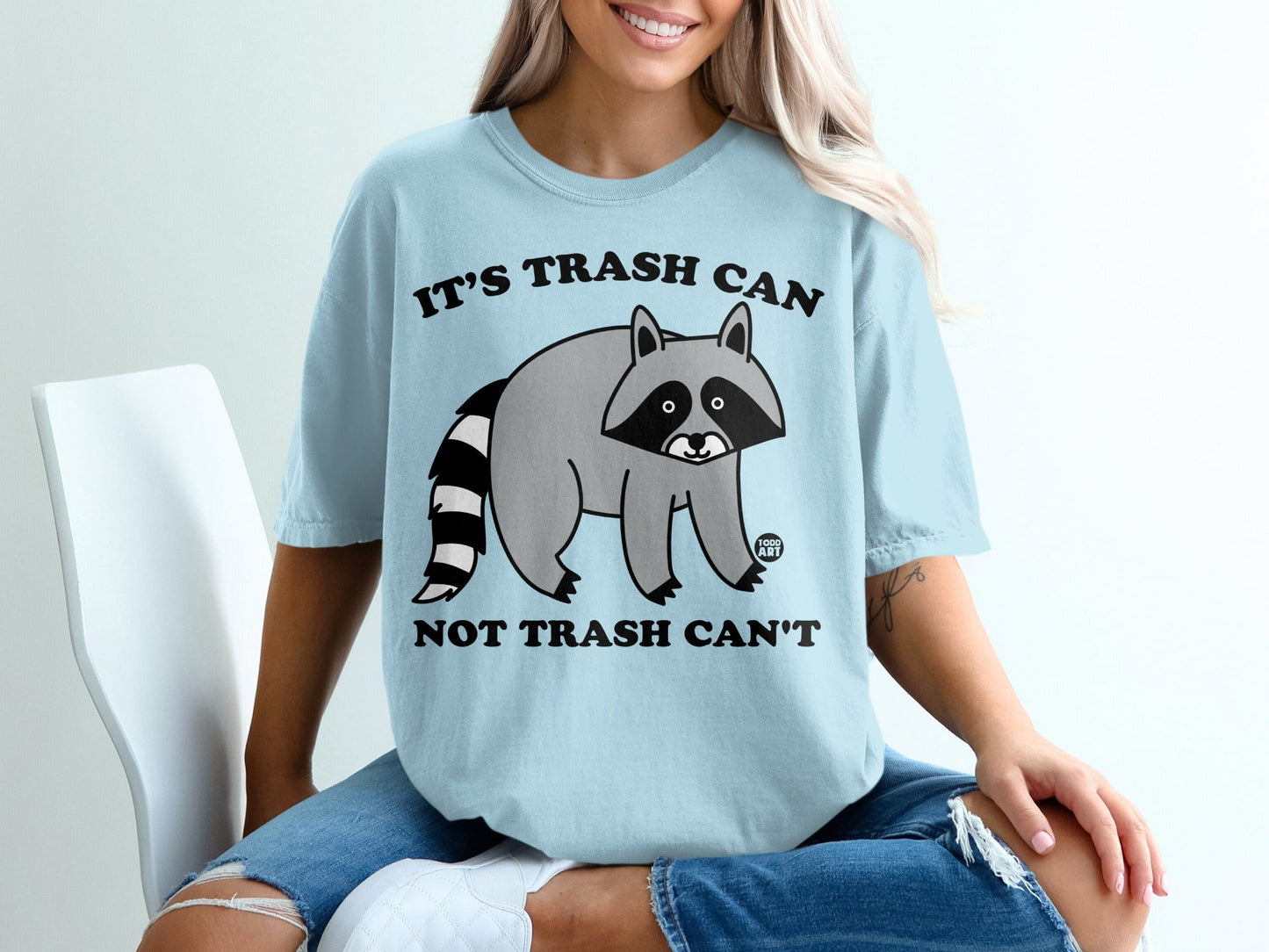 Light blue t-shirt with a raccoon and text that reads "It's trash can not trash can't".