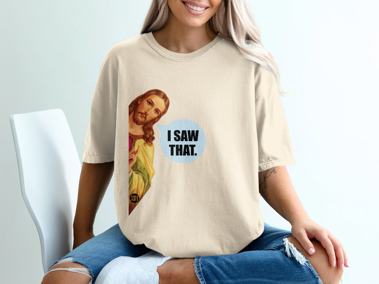 Cream t-shirt with Jesus peeking from the side saying "I SAW THAT."