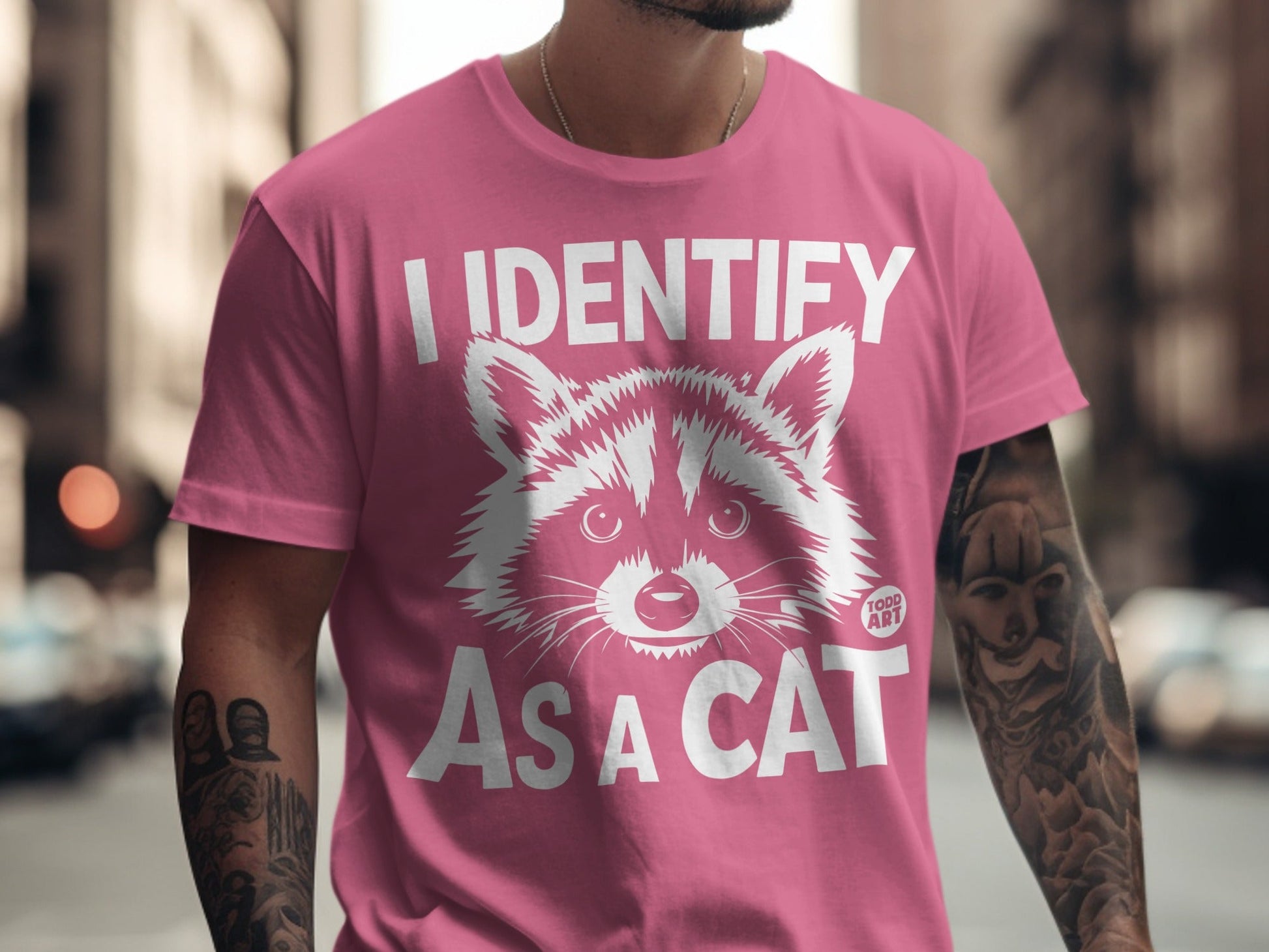Pink t-shirt with white text "I IDENTIFY AS A CAT" and a raccoon illustration.