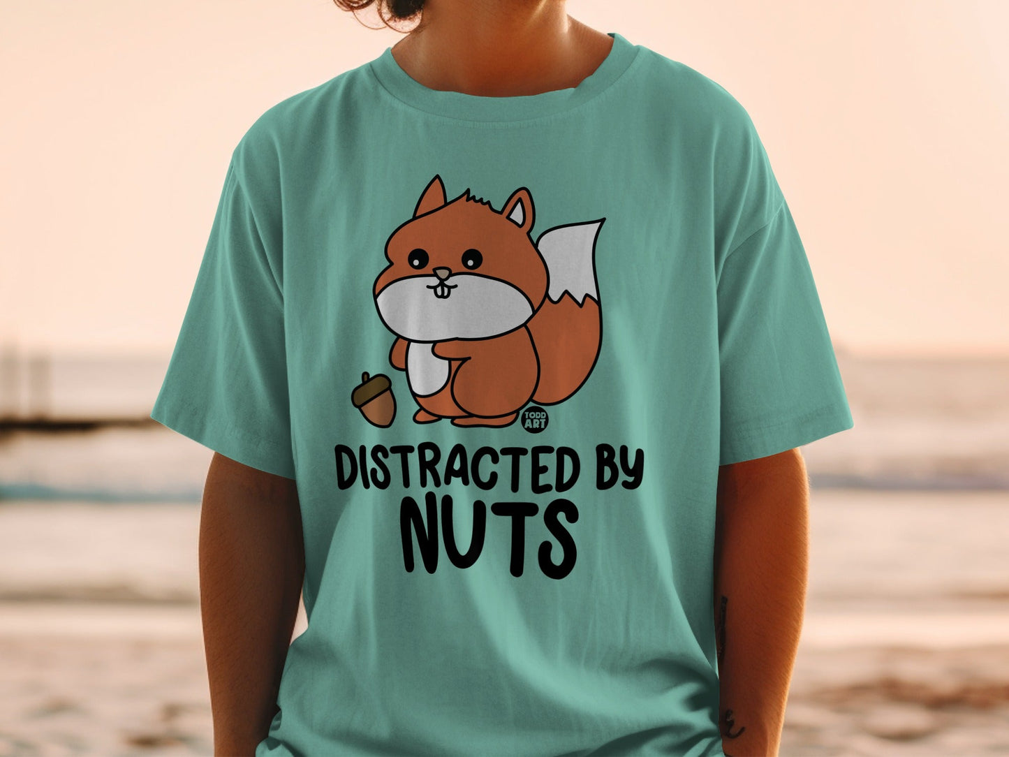 Teal t-shirt with a cartoon squirrel holding an acorn and text "DISTRACTED BY NUTS".