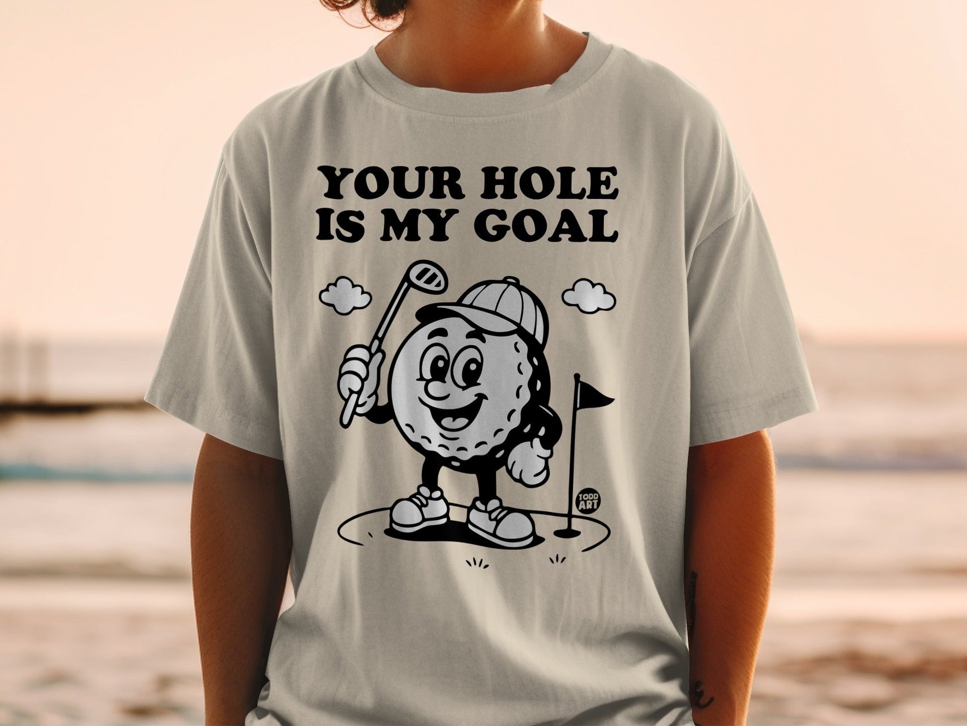 T-shirt with cartoon golf ball character holding a club, text "YOUR HOLE IS MY GOAL".
