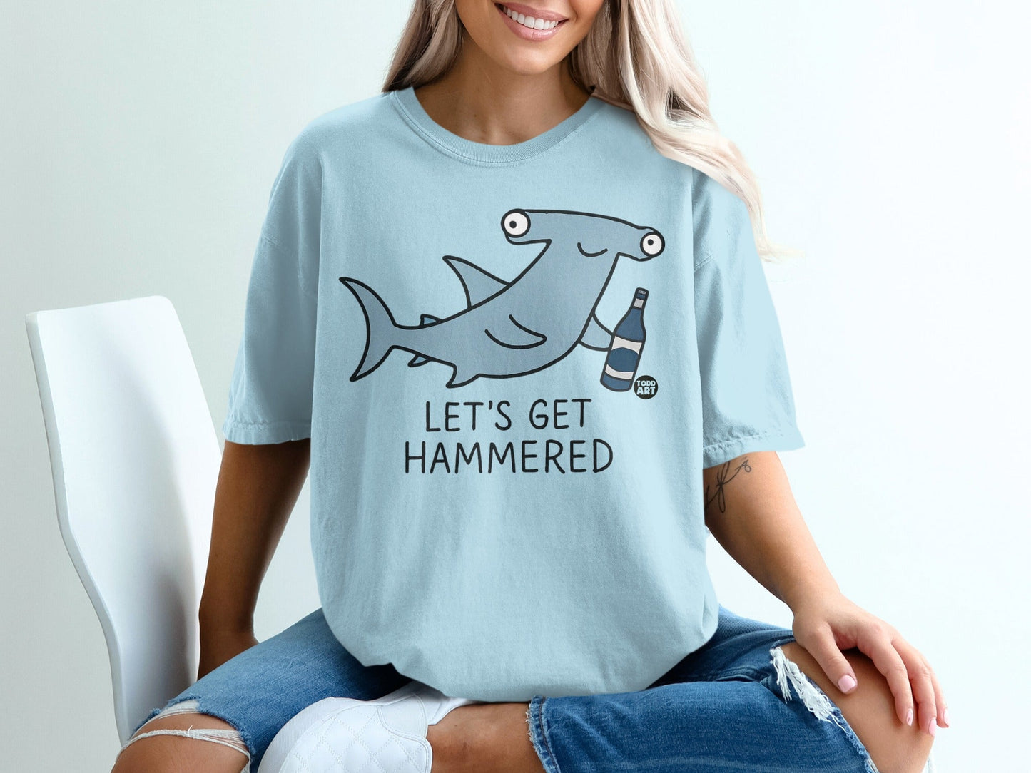 Light blue t-shirt with cartoon hammerhead shark holding a bottle, text "LET'S GET HAMMERED".