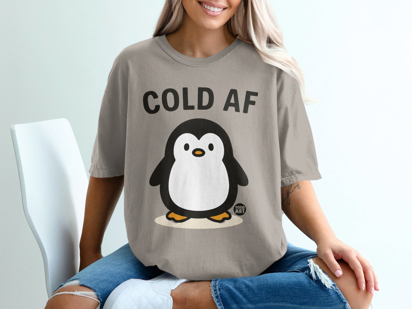 Penguin graphic with "COLD AF" text on a tan t-shirt.