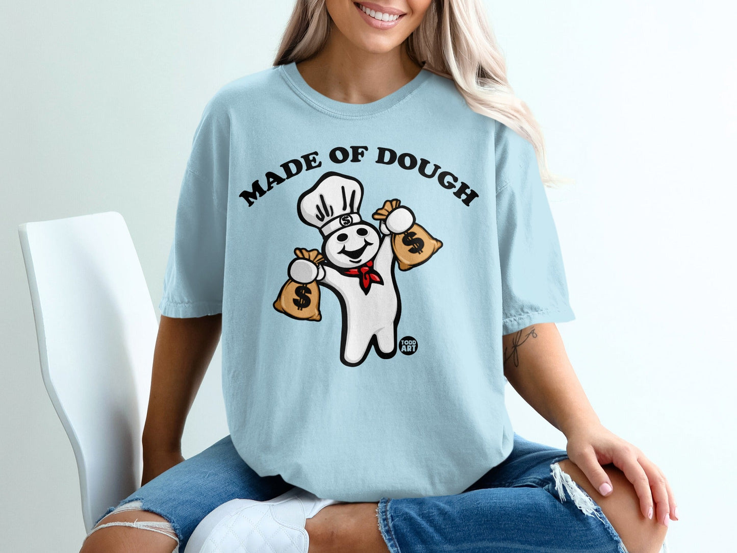Pillsbury Doughboy in chef hat holding money bags on light blue t-shirt.