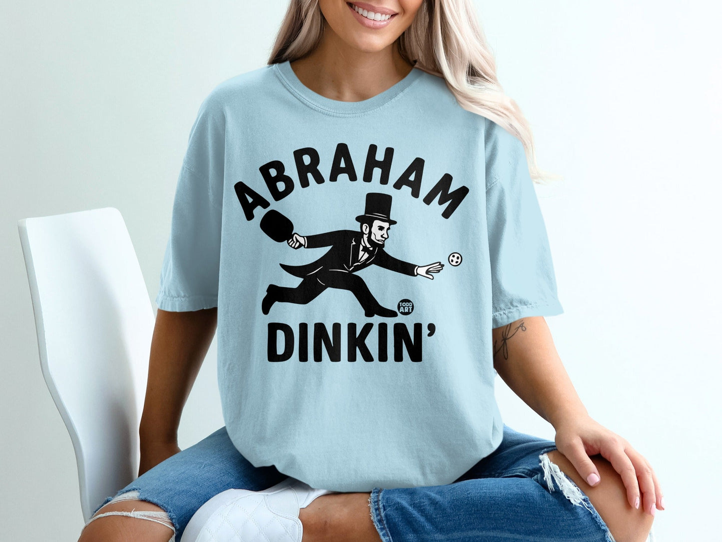 Abraham Lincoln in a suit playing badminton on a light blue t-shirt.