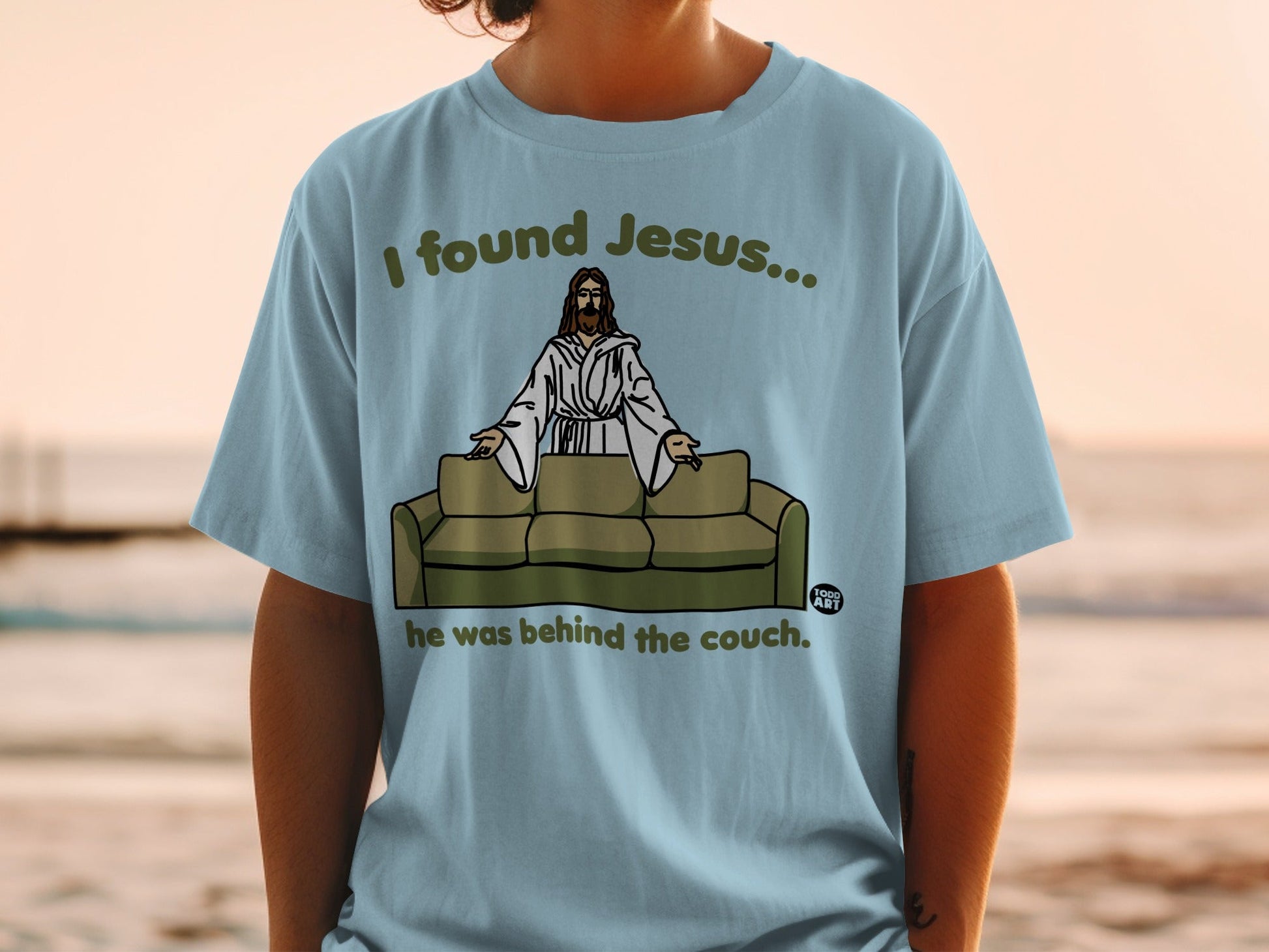 T-shirt graphic: Jesus sitting on a couch with text "I found Jesus... he was behind the couch."