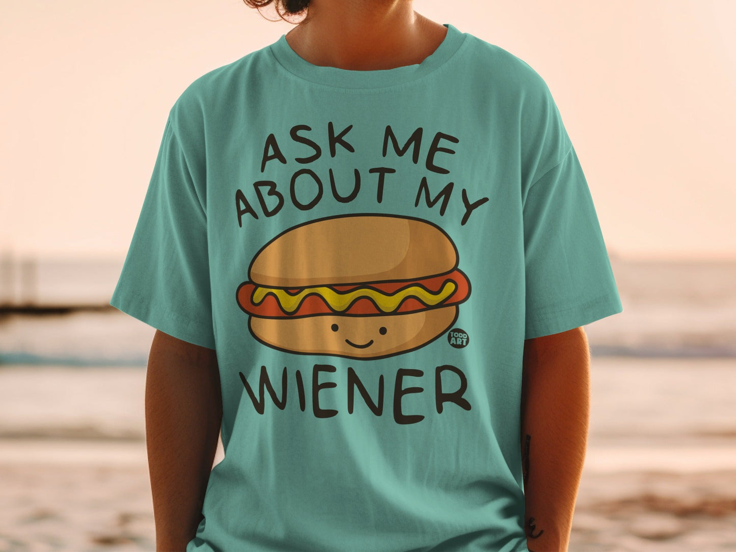 Teal t-shirt with text "ASK ME ABOUT MY WIENER" and cartoon hot dog graphic.