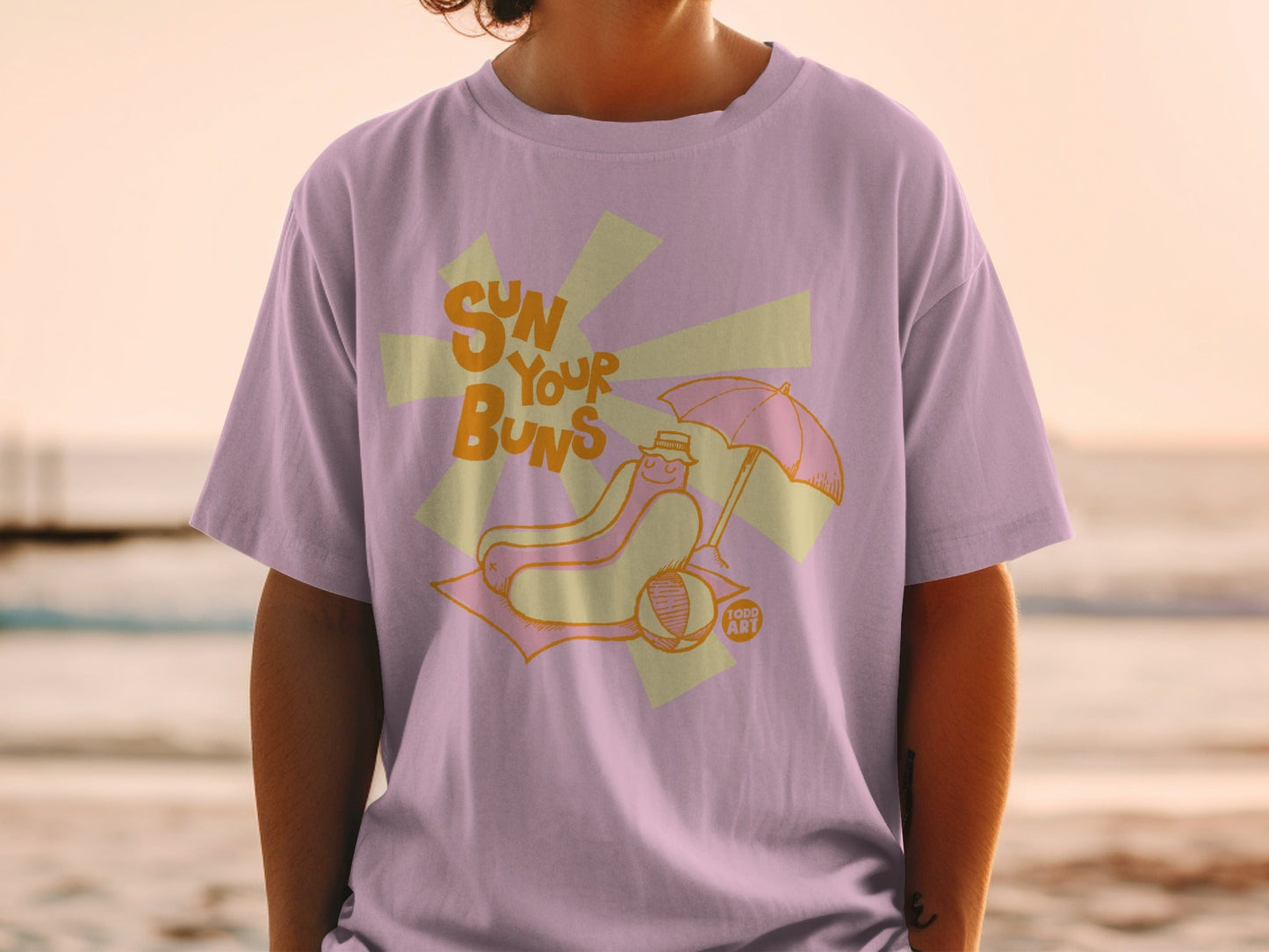 Hot dog on a beach blanket under an umbrella, text reads "SUN YOUR BUNS".