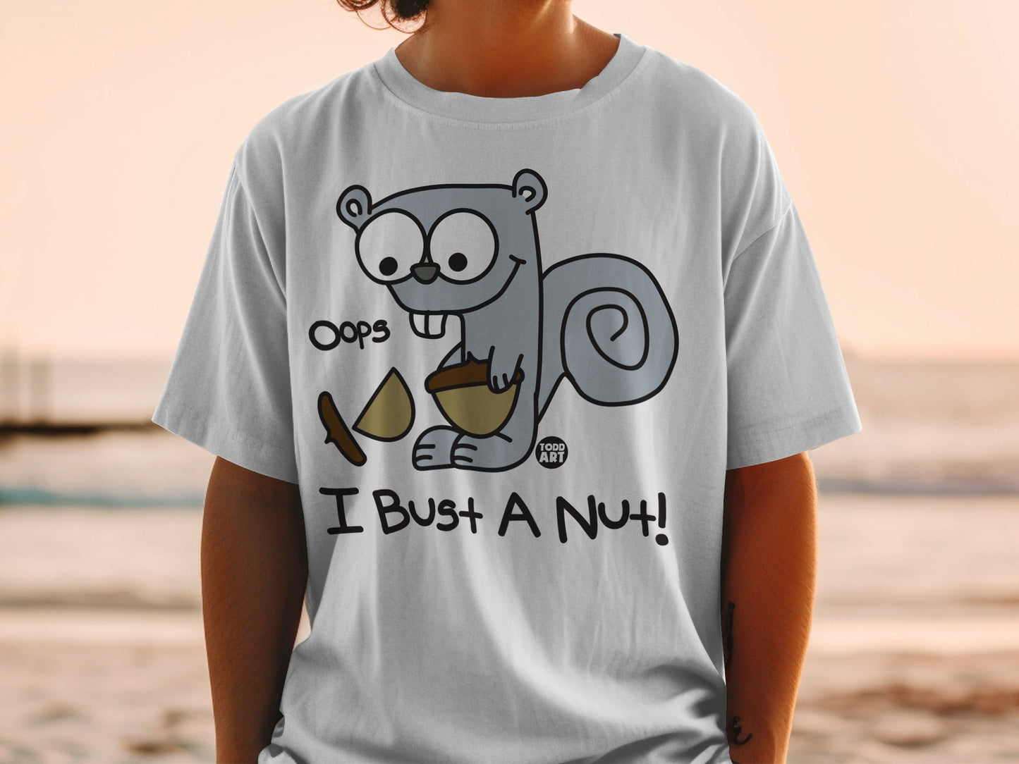 White t-shirt with cartoon squirrel holding a nut and saying "Oops I Bust a Nut!".